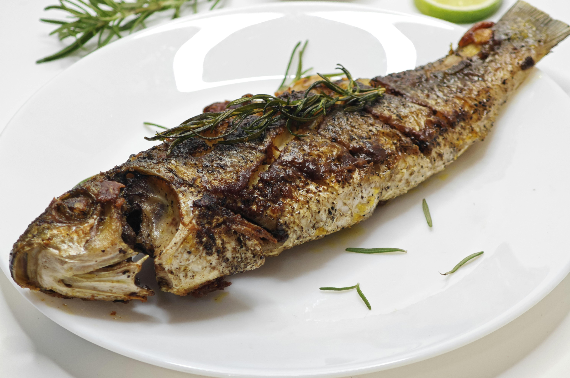 Image of Pro Chefly grilled whole trout with herb butter and fresh rosemary on a white serving plate.