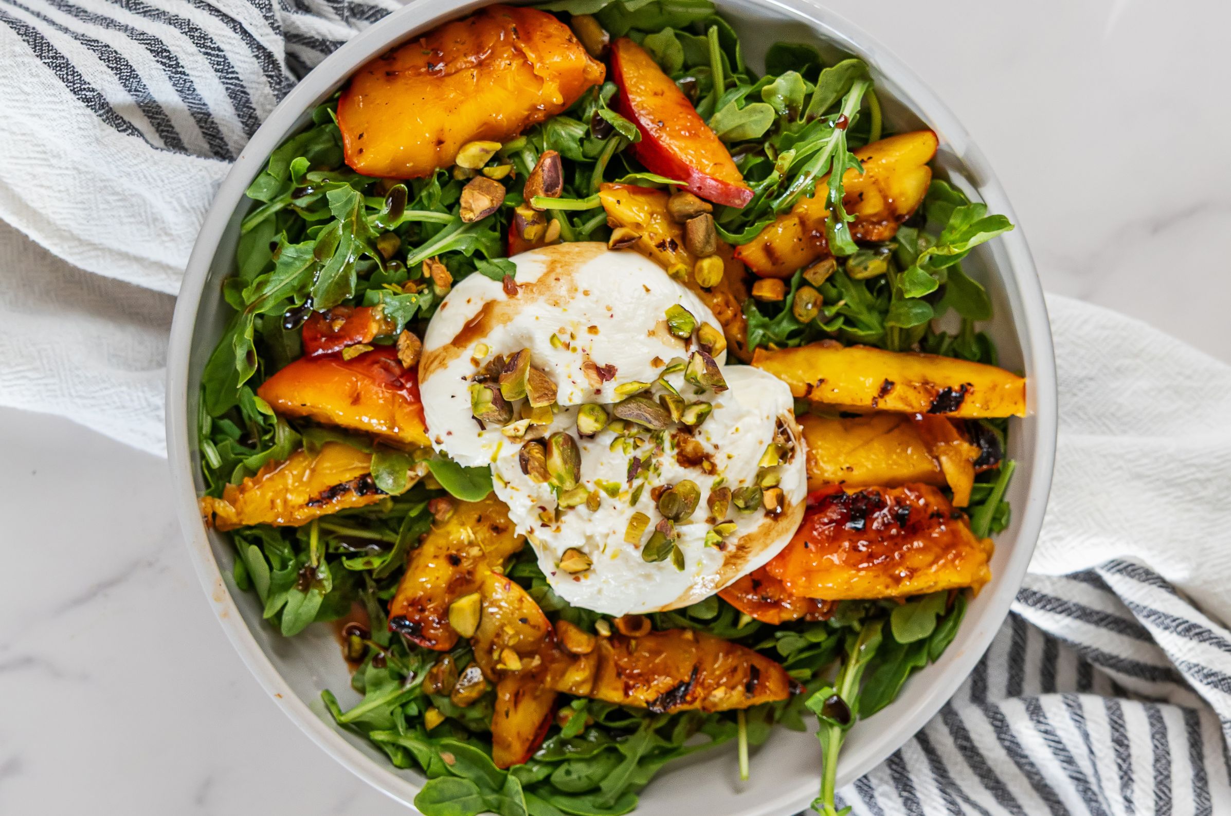 Image of Pro Chefly grilled peach and burrata salad with arugula, pistachios, balsamic glaze, and fresh peaches.