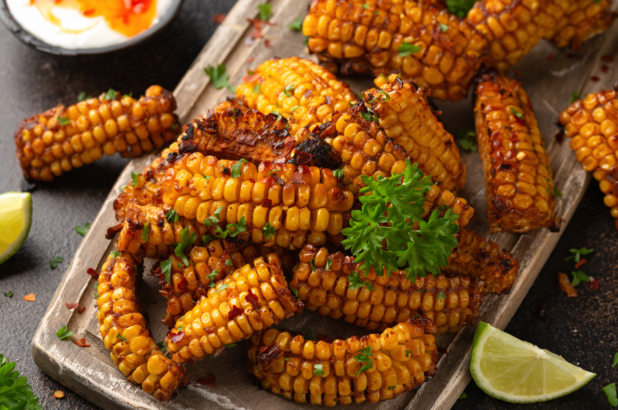 Image of Pro Chefly spicy grilled corn ribs with chili seasoning, fresh parsley, lime wedges, and creamy dipping sauce.