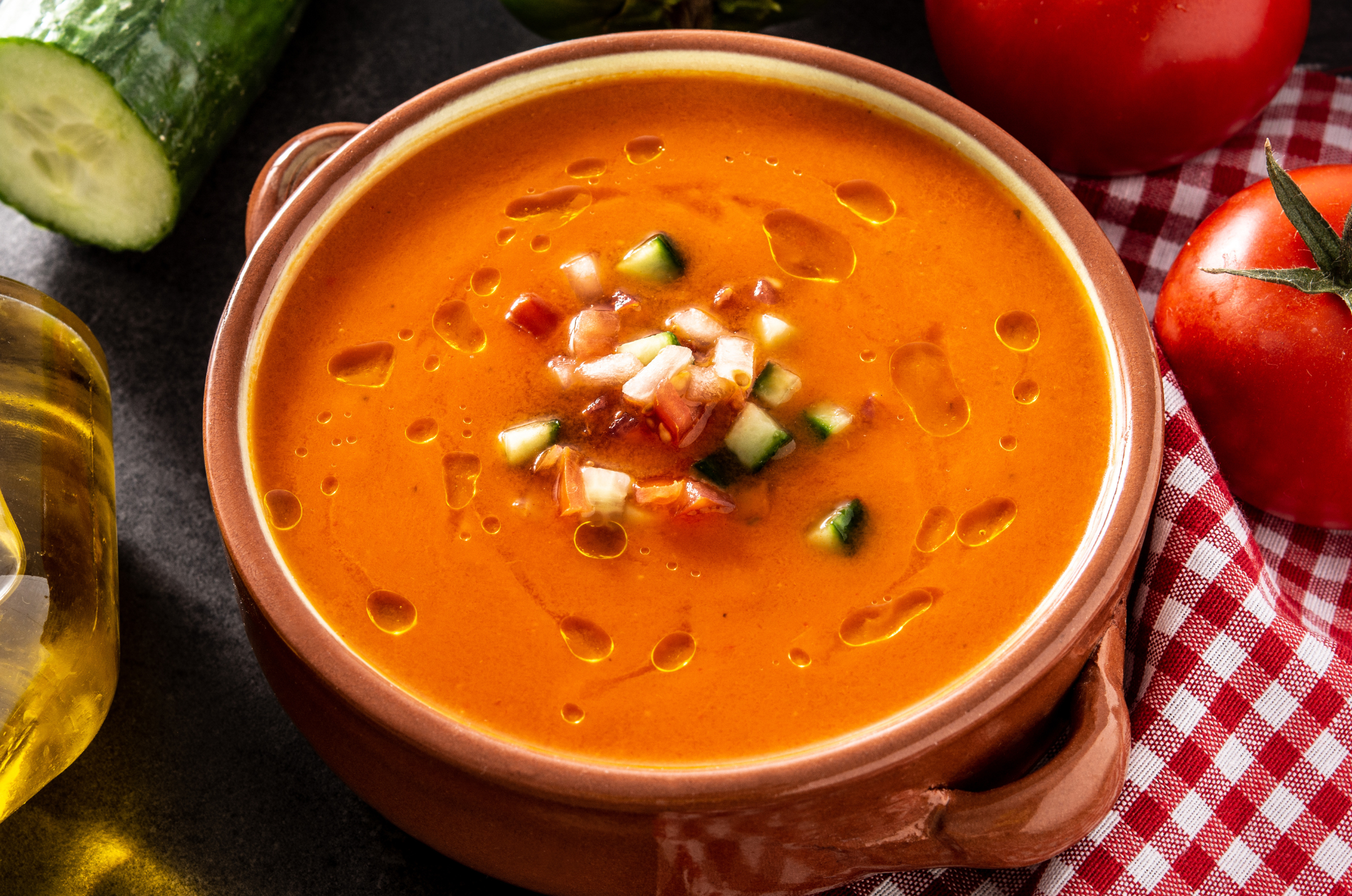 Image of Pro Chefly traditional gazpacho topped with diced cucumber, tomato, onion, and olive oil in a rustic bowl.