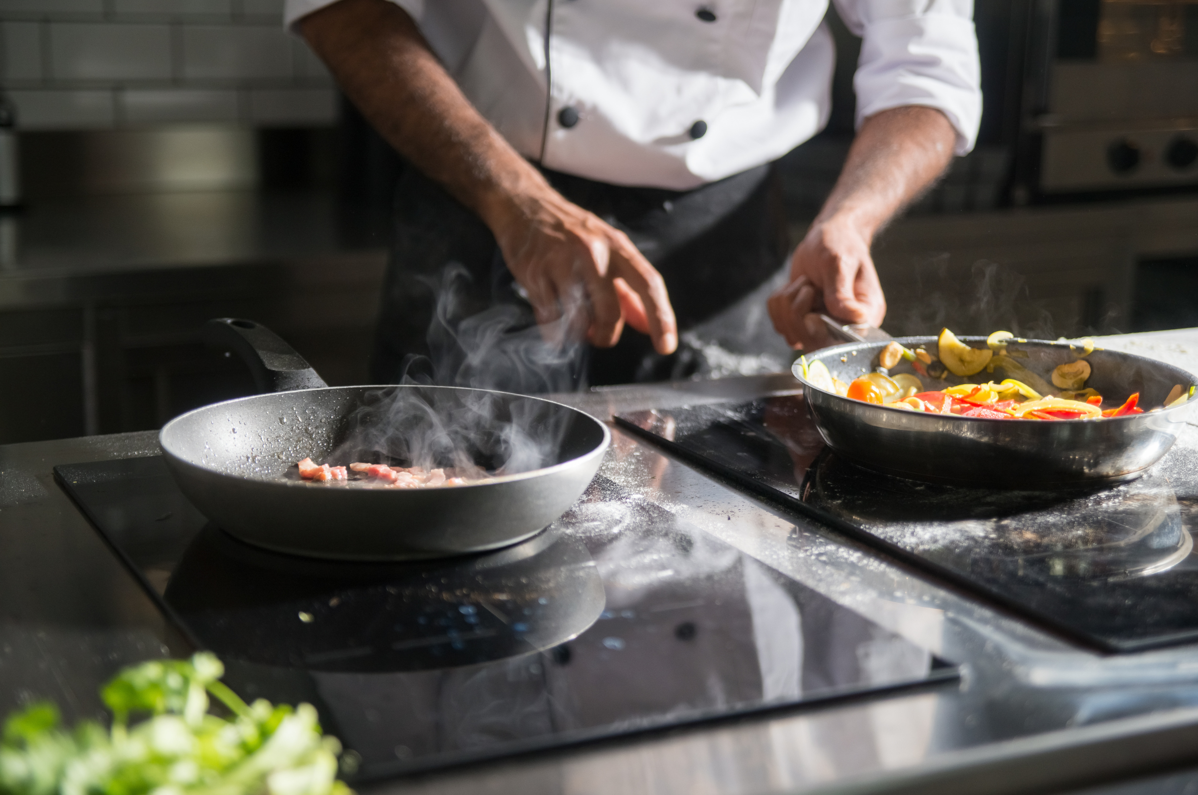 Image of Pro Chefly chef sautéing vegetables while searing ingredients in a professional kitchen on a stovetop.