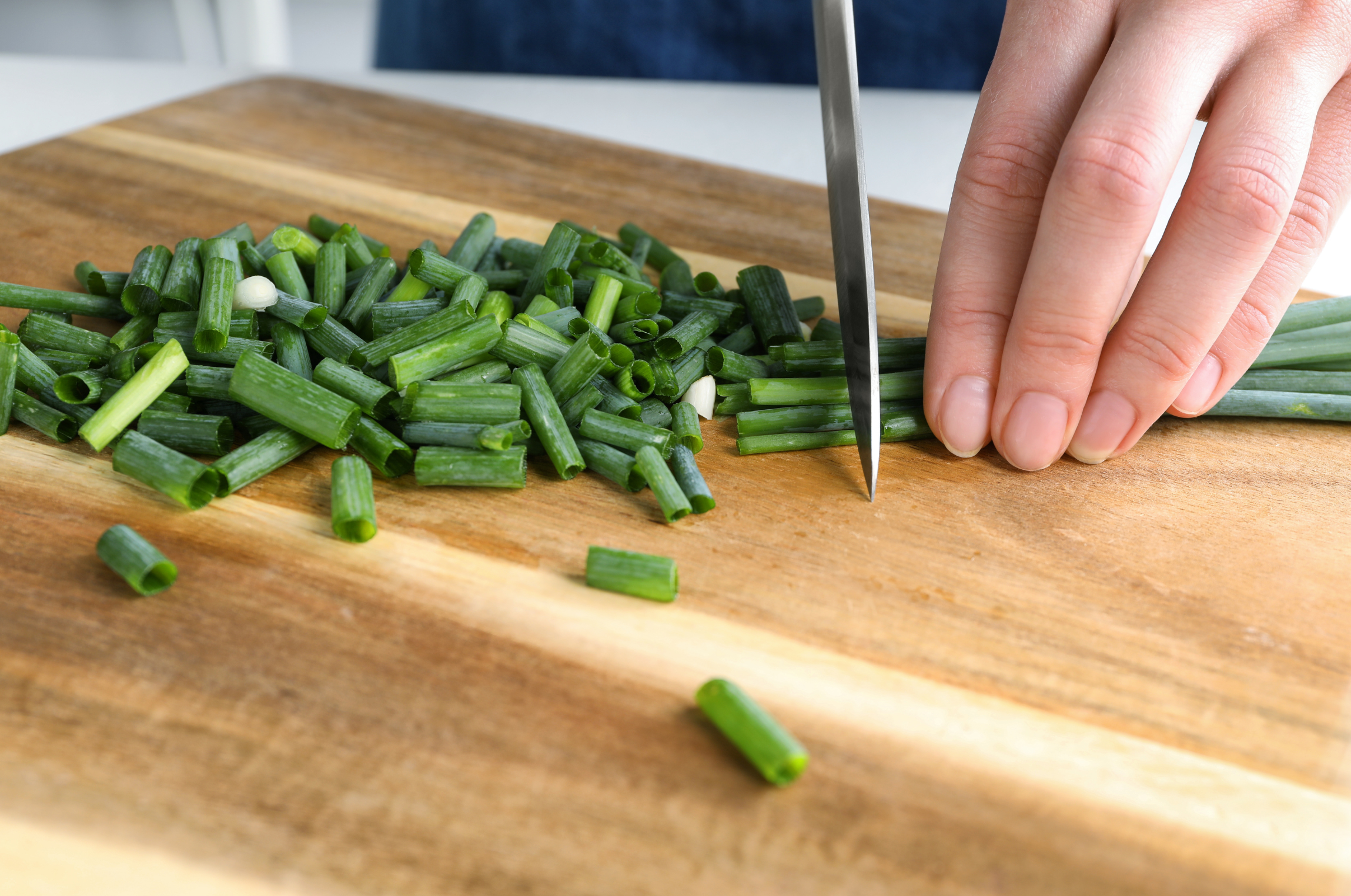 Image of Pro Chefly sharp Japanese knife slicing fresh green onions on a wooden cutting board using proper pinch grip technique for precise vegetable prep.