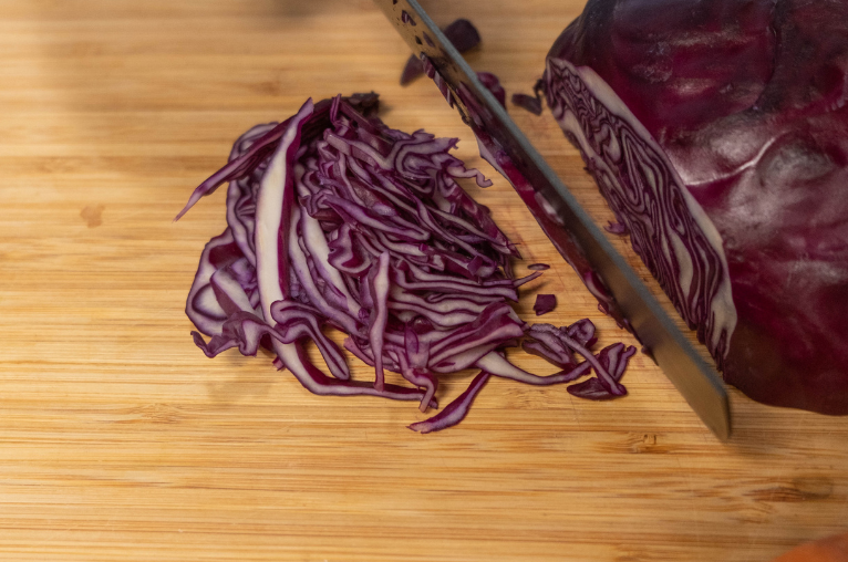 Image of Pro Chefly Japanese Damascus knife slicing red cabbage on a wooden cutting board, highlighting clean cuts and precise vegetable prep.