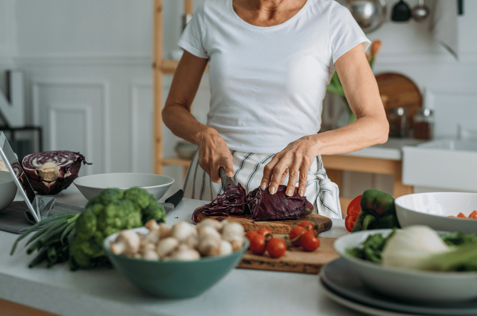 Image of Pro Chefly Japanese Damascus chef knife slicing fresh red cabbage on a wooden cutting board surrounded by vegetables in a home kitchen.