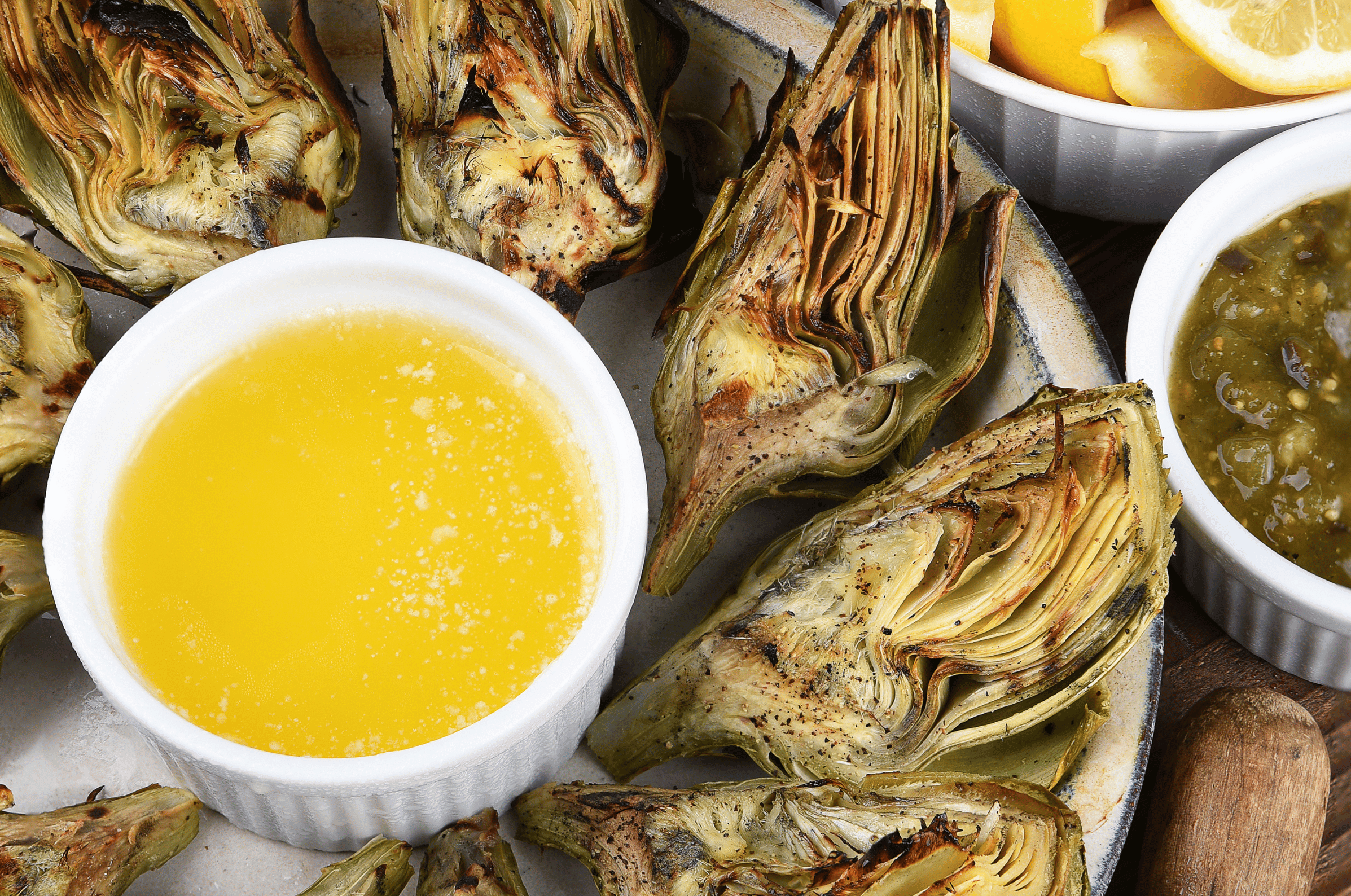 Image of Pro Chefly grilled artichokes served with melted butter and lemon dipping sauce on a rustic platter.