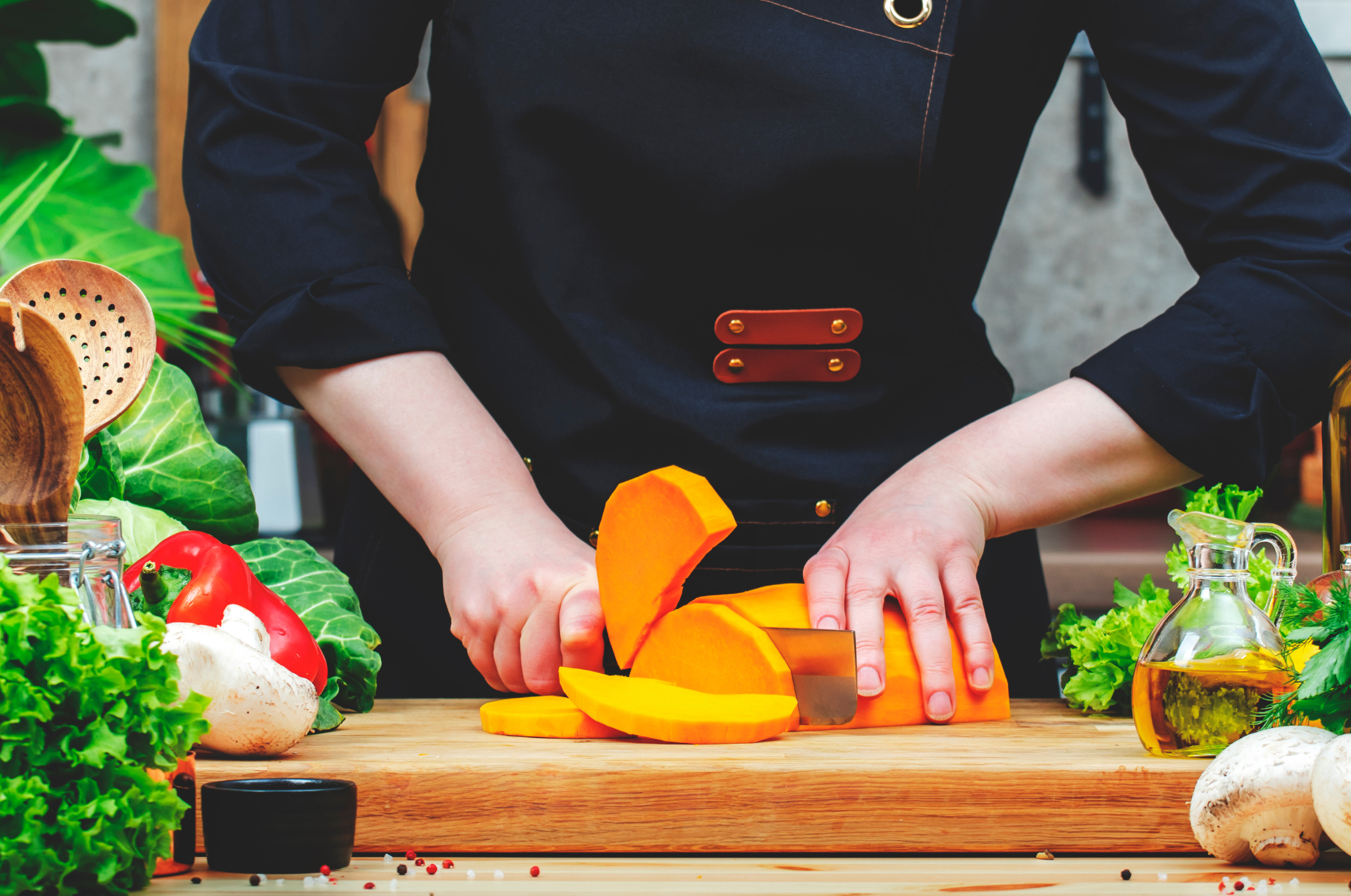 Pro Chefly chef slicing bright orange squash with a Japanese kitchen knife on a wooden board, surrounded by fresh vegetables and herbs for premium meal prep.