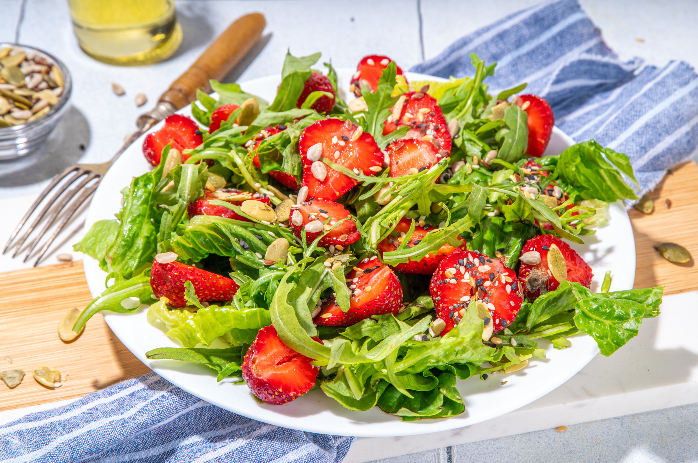 Image of Pro Chefly strawberry arugula salad with mixed greens, sliced strawberries, and toasted seeds served on a white plate.