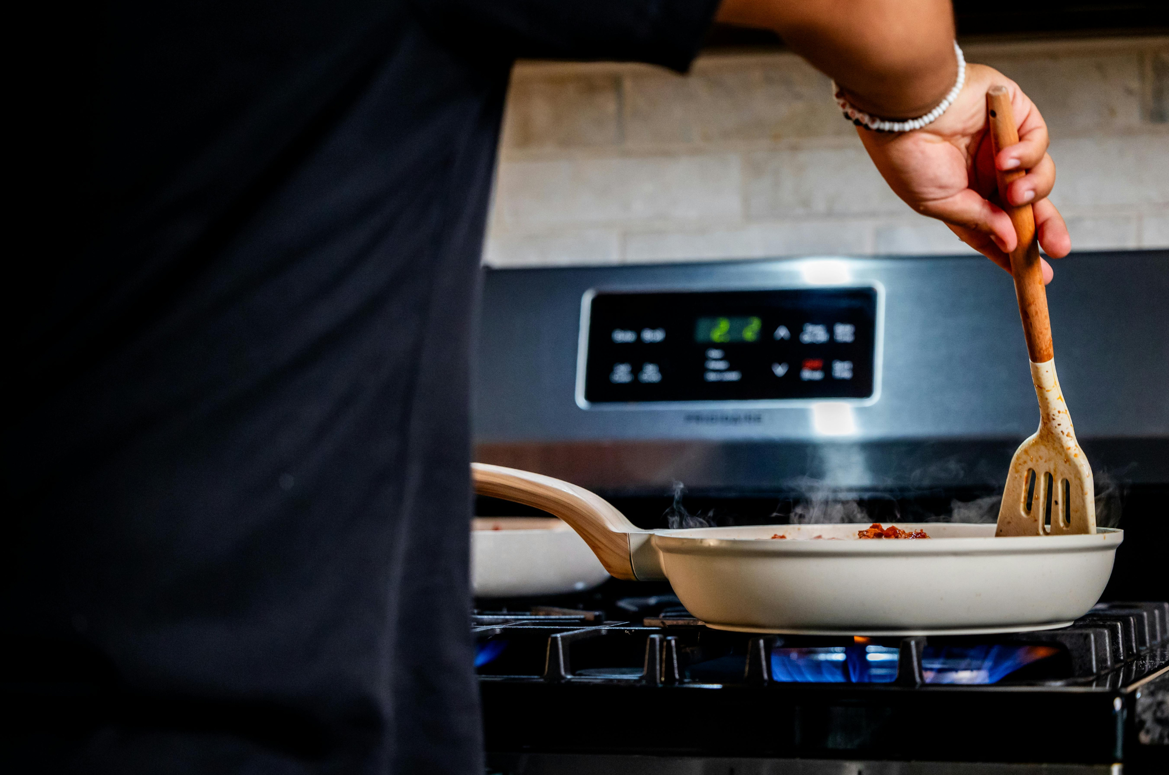 Image of Pro Chefly stovetop cooking scene with a pan over an open flame, chef stirring food with a wooden utensil, showcasing heat control, active cooking, and a modern kitchen setting