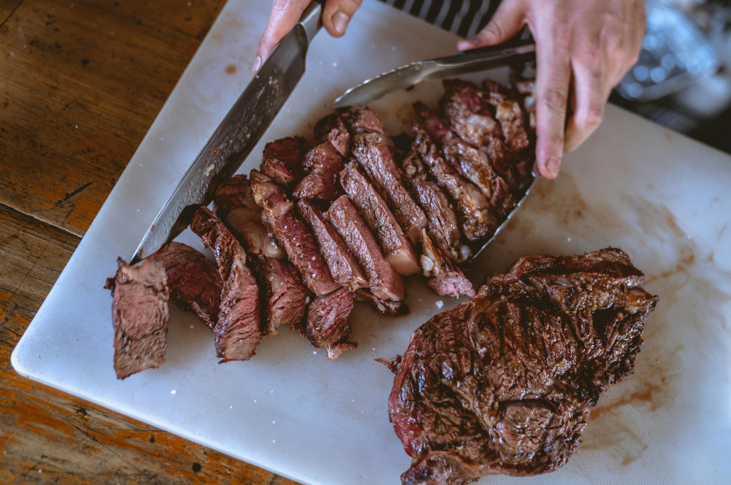Image of Pro Chefly Japanese Damascus chef knife slicing a perfectly cooked steak on a cutting board, showcasing juicy interior, clean cuts, and precision carving in a rustic kitchen setting