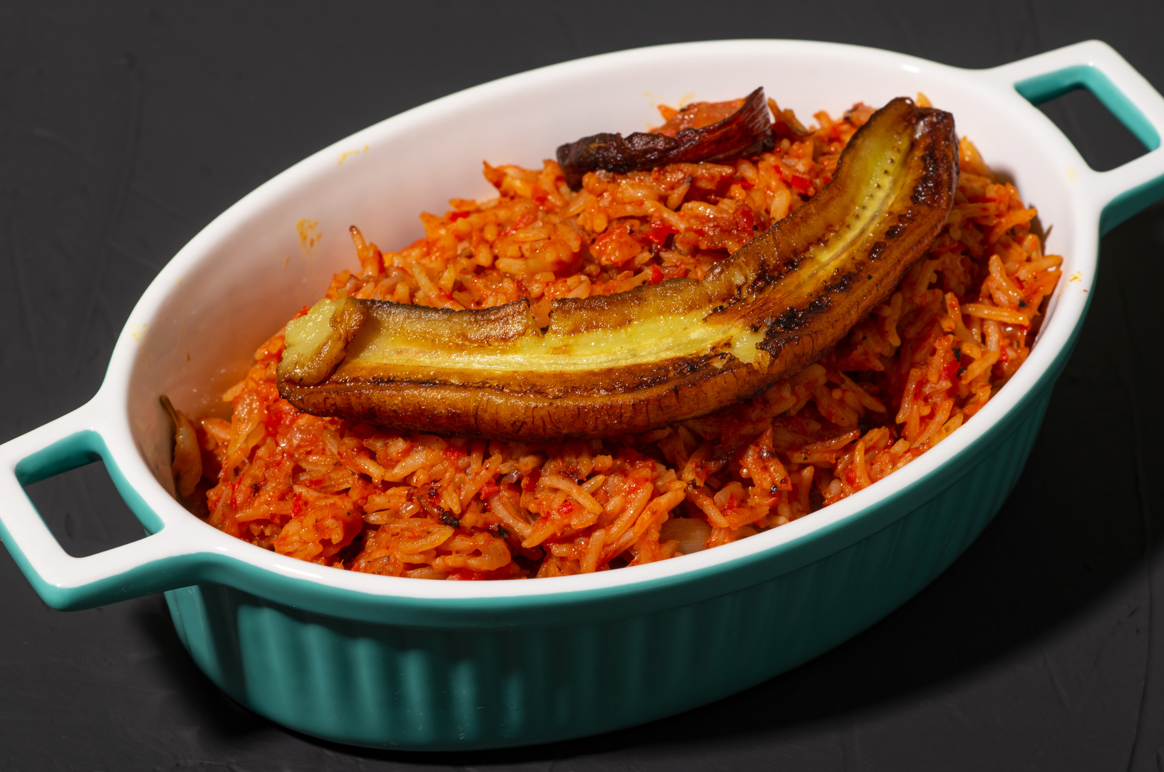 Image of Pro Chefly Nigerian jollof rice served in a ceramic dish, topped with caramelized fried plantain.