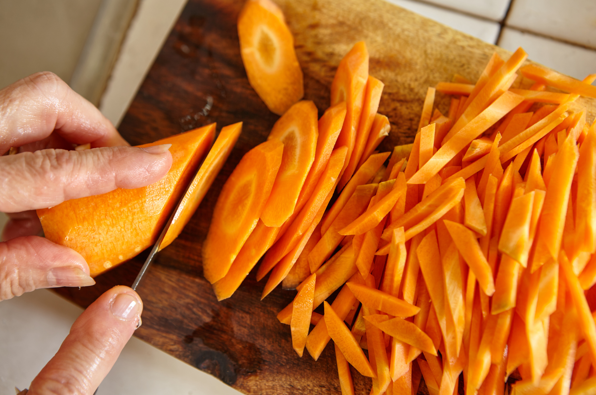 Image of Pro Chefly Japanese knives slicing fresh carrots into thin julienne cuts on a wooden cutting board.