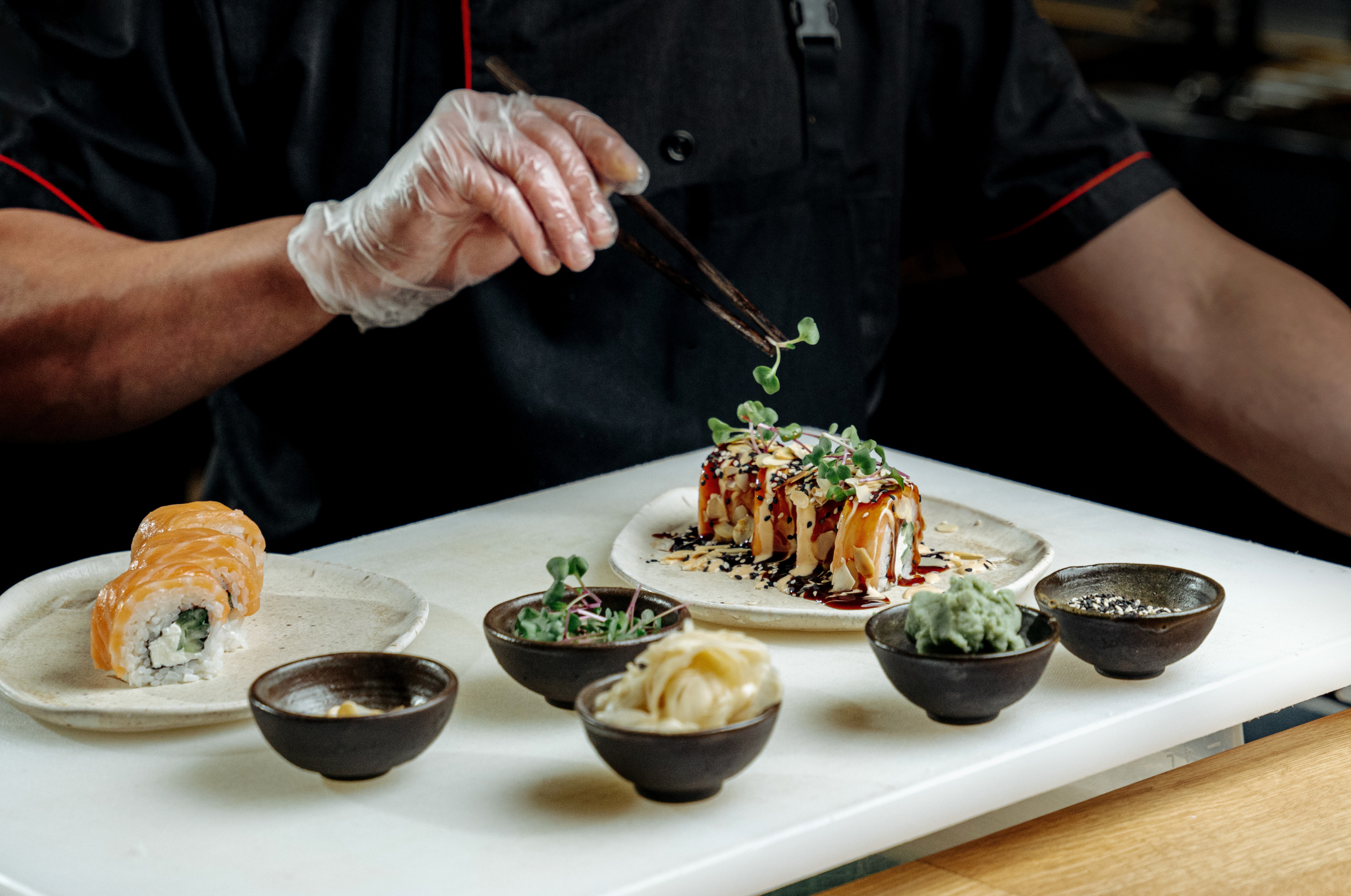 Image of Pro Chefly sushi plating with chef finishing a specialty sushi roll using microgreens and sauces on a restaurant prep station.