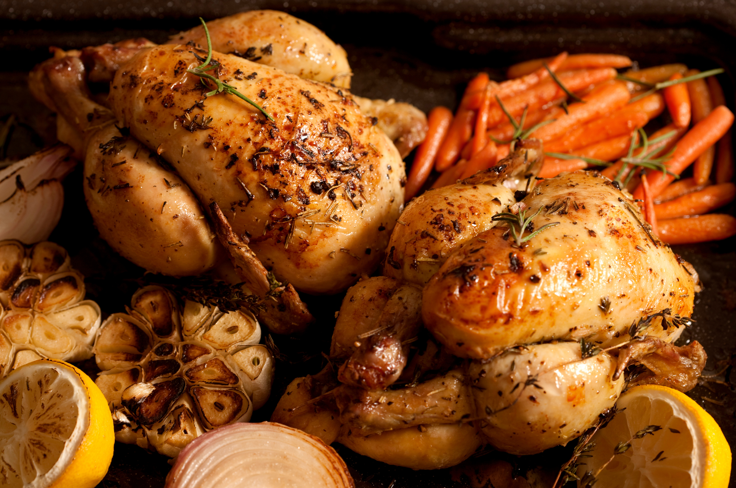 Image of Pro Chefly herb-roasted whole chickens with carrots, garlic, onions, and lemon on a rustic roasting tray, golden crispy skin and rich caramelization