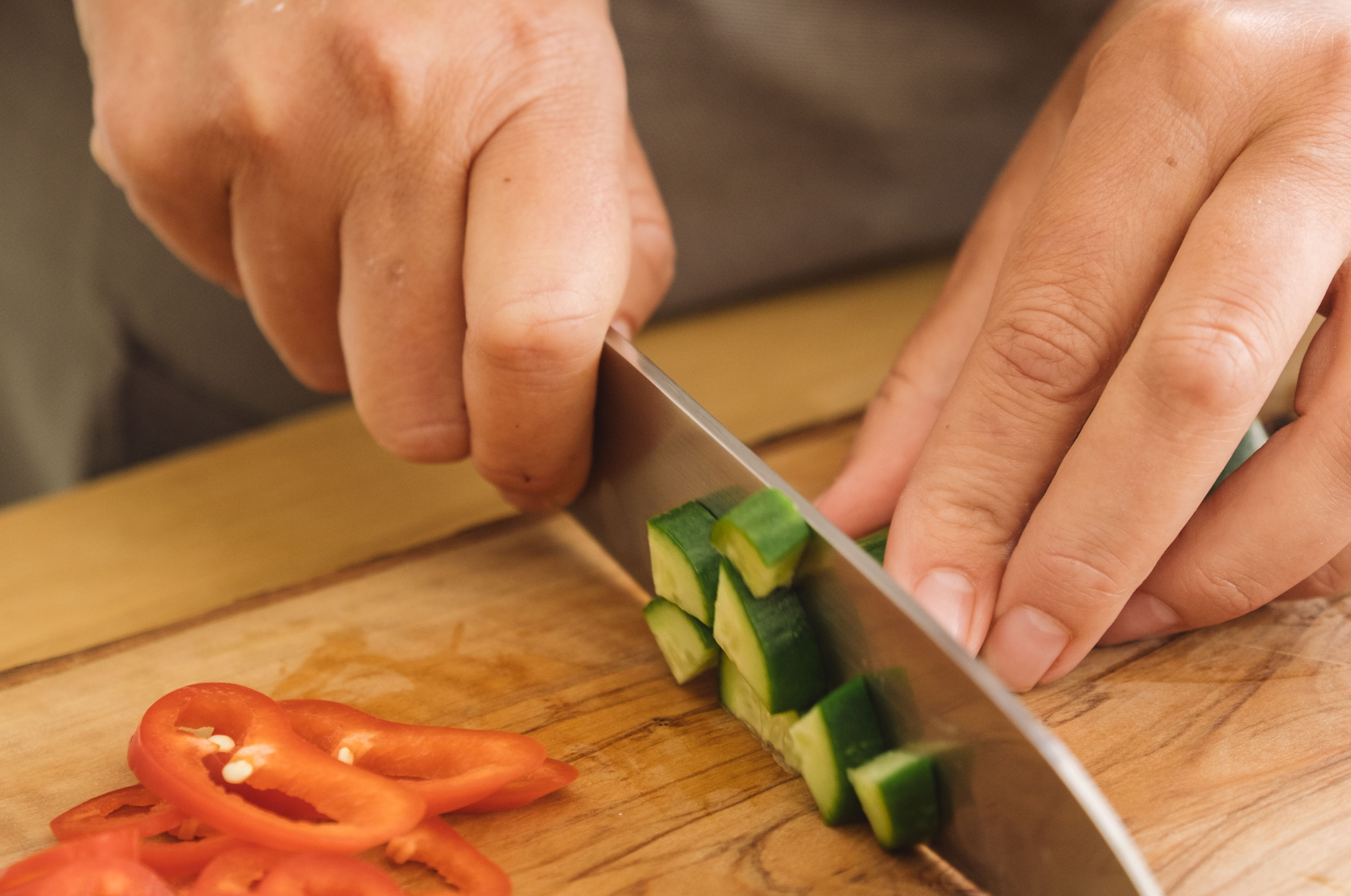 Image of Pro Chefly chef dicing cucumber and slicing pepper with a Japanese Damascus knife on a wooden cutting board.