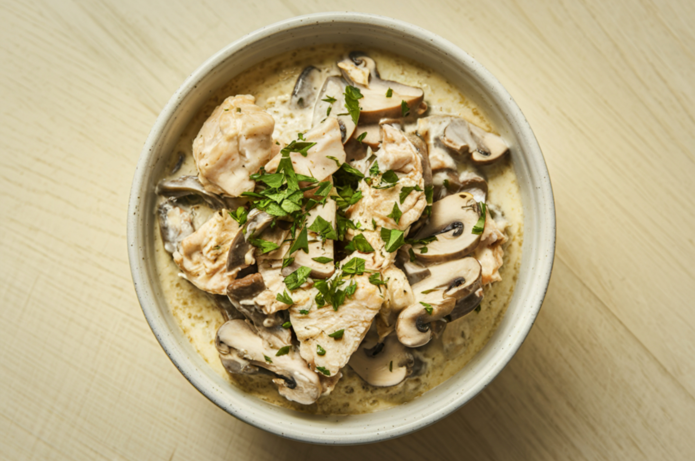 Image of Pro Chefly creamy chicken and mushroom dish finished with fresh herbs, served in a ceramic bowl.