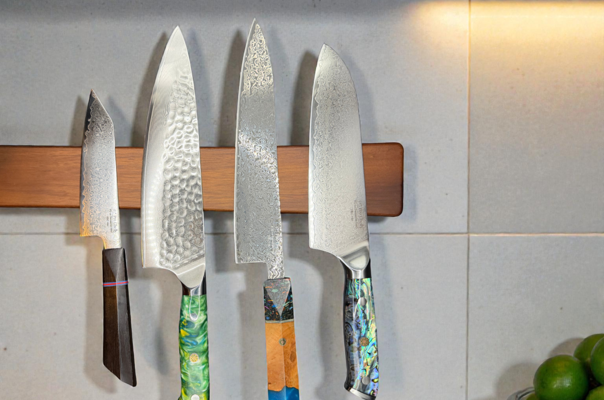 Image of Pro Chefly Damascus and Japanese knives displayed on a magnetic wall strip, featuring chef knife, santoku, and paring knife with patterned blades and artisan handles for precision kitchen performance