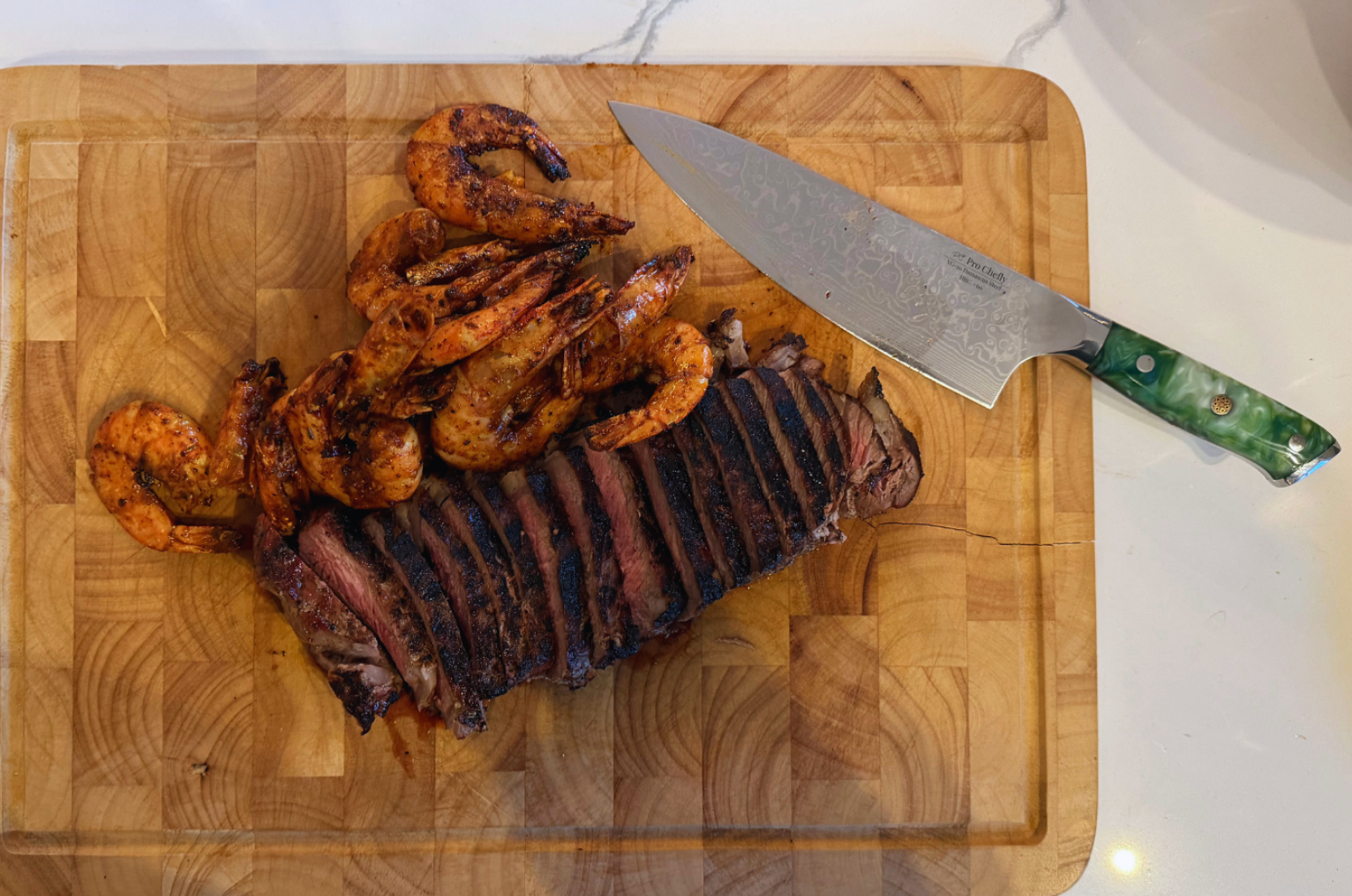 Image of Pro Chefly Damascus chef knife with grilled steak and shrimp on a wooden cutting board, showcasing precision, balance, and Japanese knife craftsmanship.