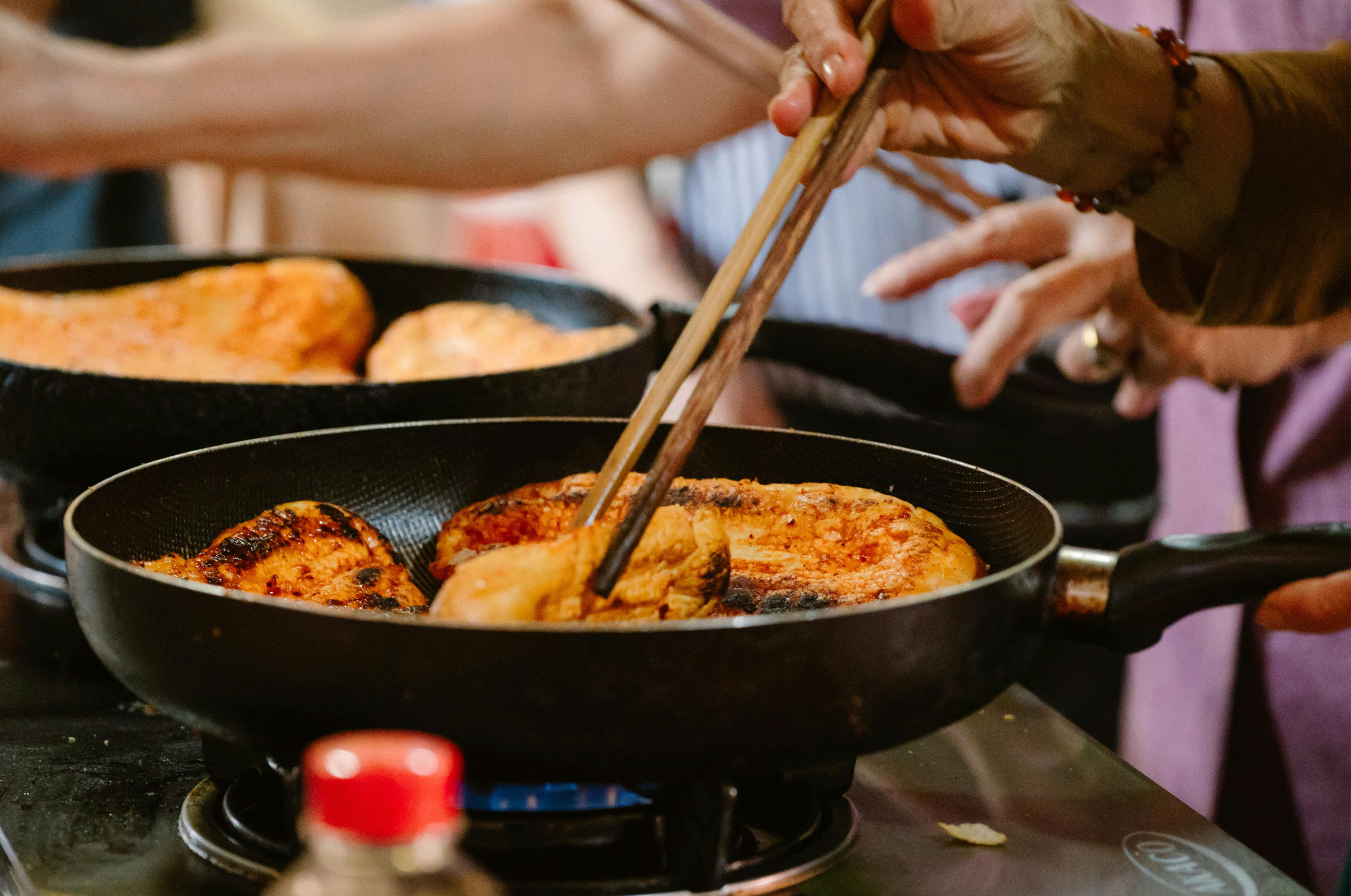 Image of Pro Chefly chefs pan-searing chicken in a skillet, hands-on cooking with precise heat control, showcasing professional kitchen technique and culinary craftsmanship.