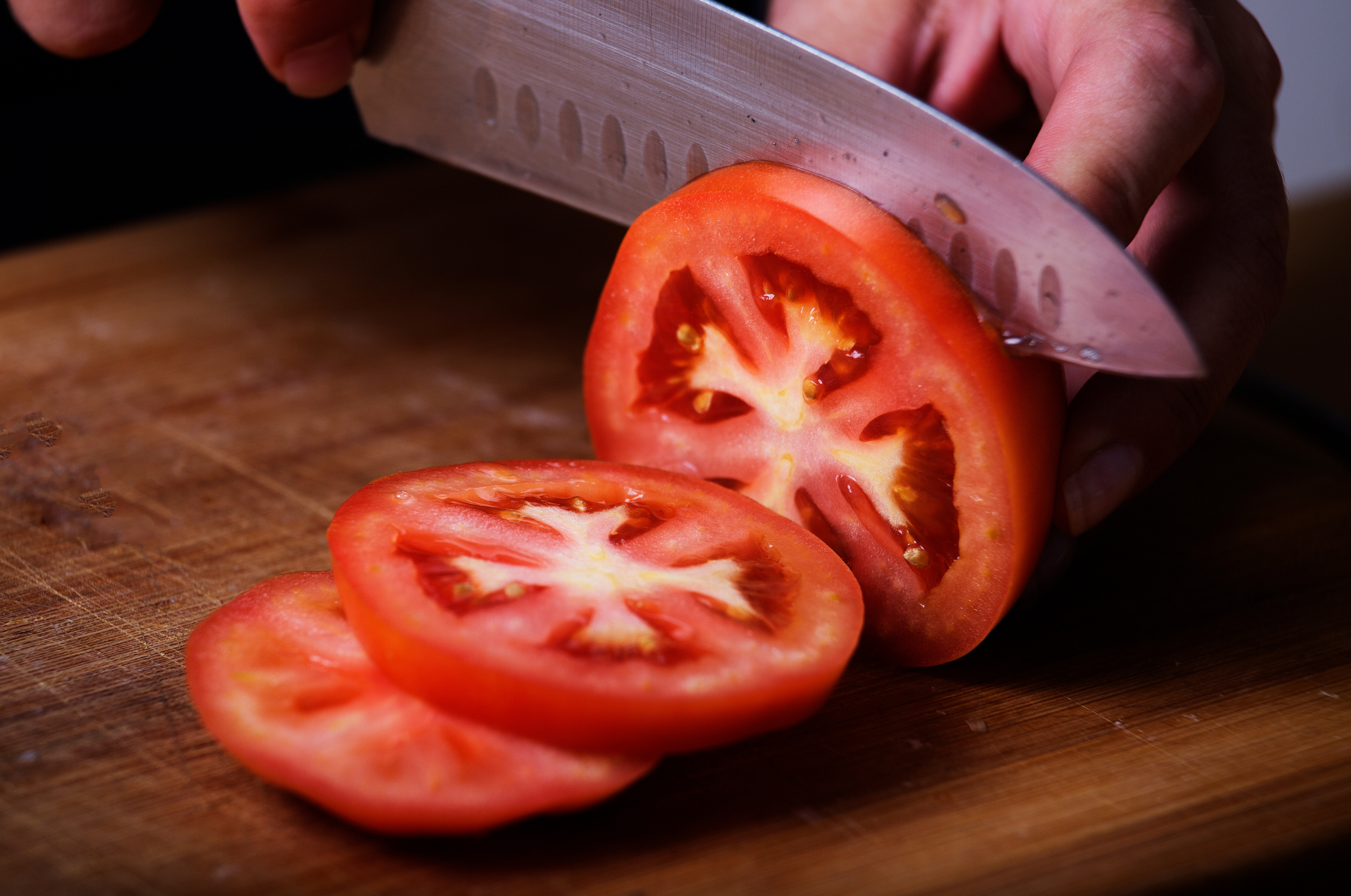 Image of Pro Chefly Japanese Damascus chef knife slicing a ripe tomato on a wooden cutting board, showcasing precise cuts, sharp blade control, and clean kitchen prep in warm lighting