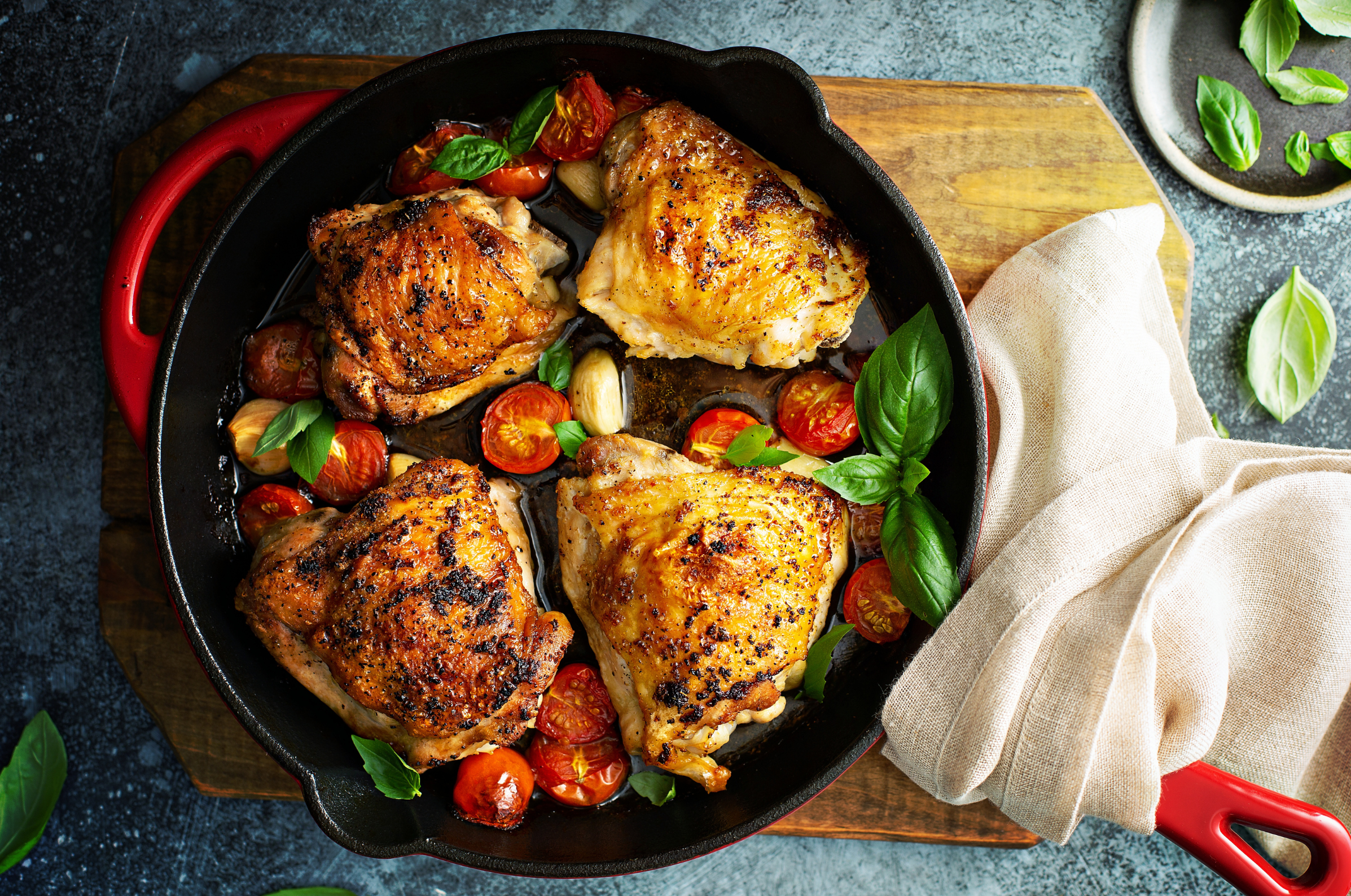 Image of Pro Chefly crispy cast-iron chicken thighs with roasted cherry tomatoes, garlic, and fresh basil.