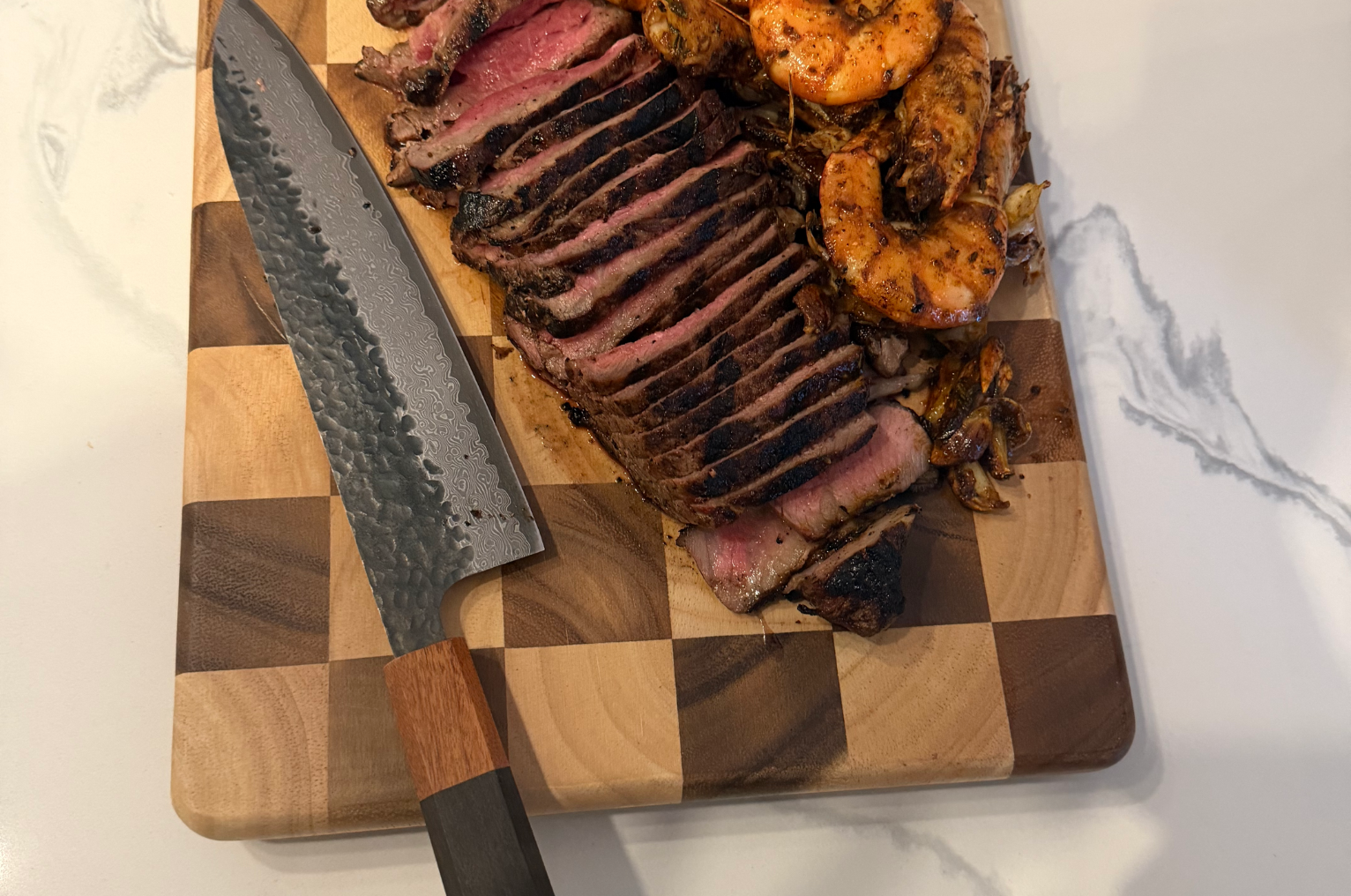 Image of Pro Chefly Damascus chef knife resting beside sliced steak and seared shrimp on a wooden cutting board, highlighting Japanese knives precision and clean protein prep.