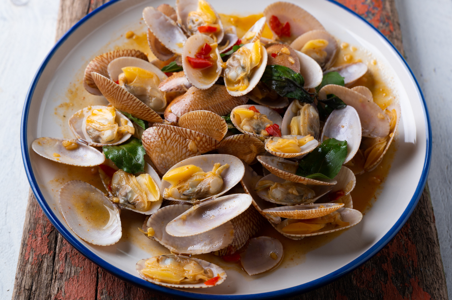 Image of Pro Chefly saffron braised clams with citrus zest, featuring tender clams in golden saffron broth with garlic, chili, and fresh herbs on a rustic plate