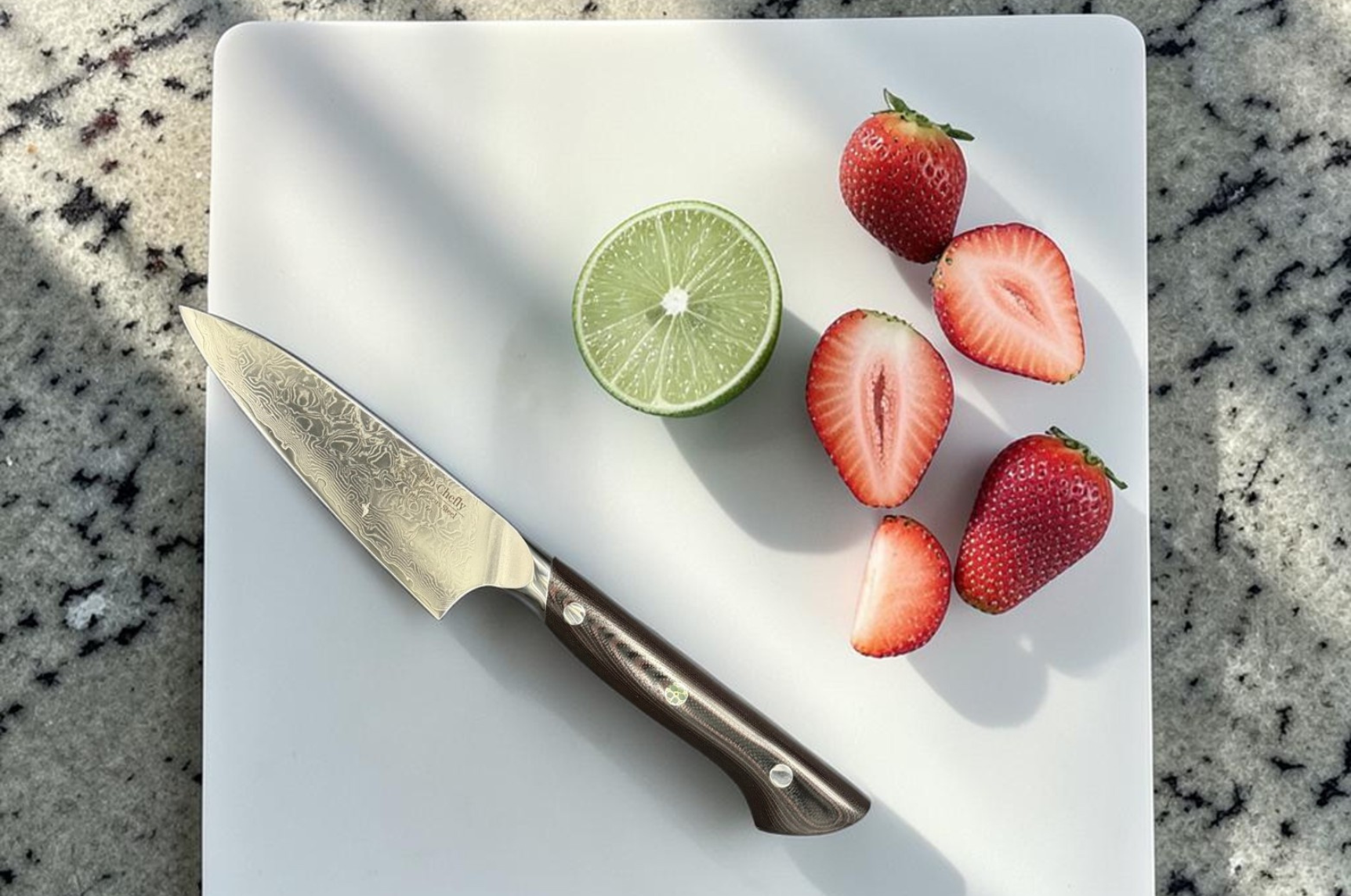 Image of Pro Chefly Japanese Damascus paring knife on a white cutting board with fresh strawberries and lime, showcasing precision craftsmanship, fine blade detail, and bright fruit prep in natural lighting