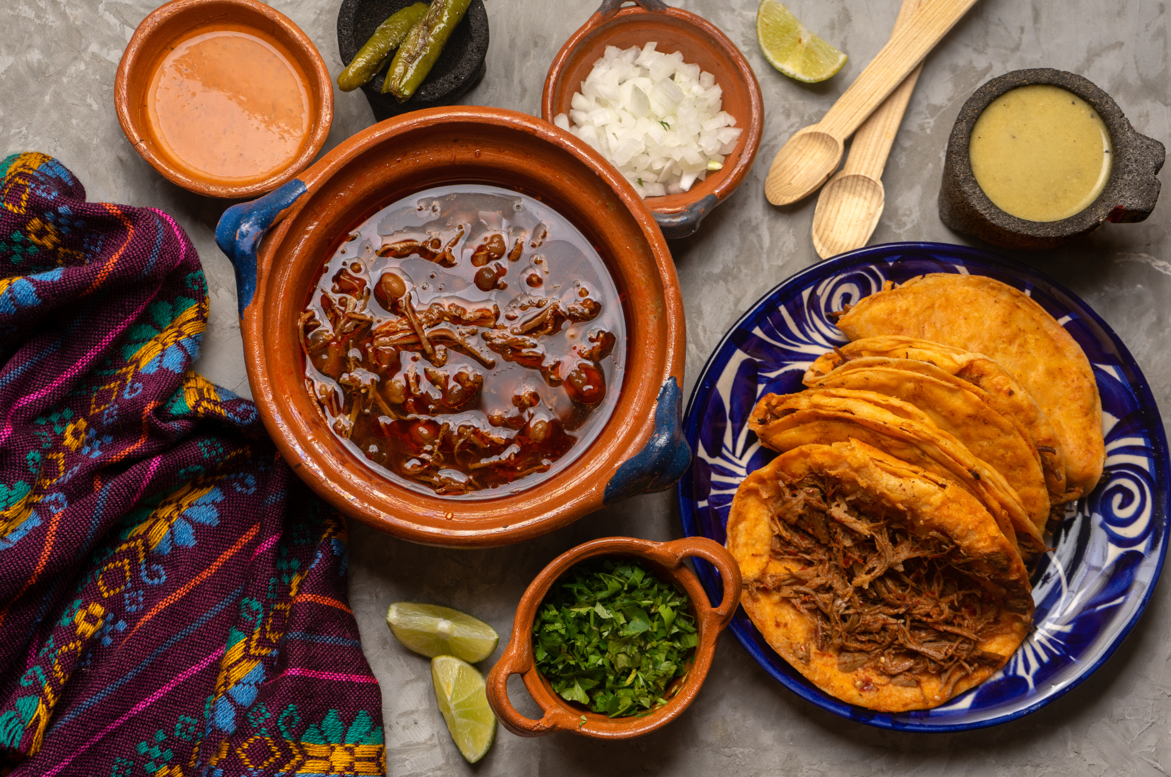 Image of Pro Chefly crispy birria tacos with shredded slow-braised beef, rich red consomé, fresh cilantro, diced onion, and lime wedges served in rustic clay bowls for Cinco de Mayo dining