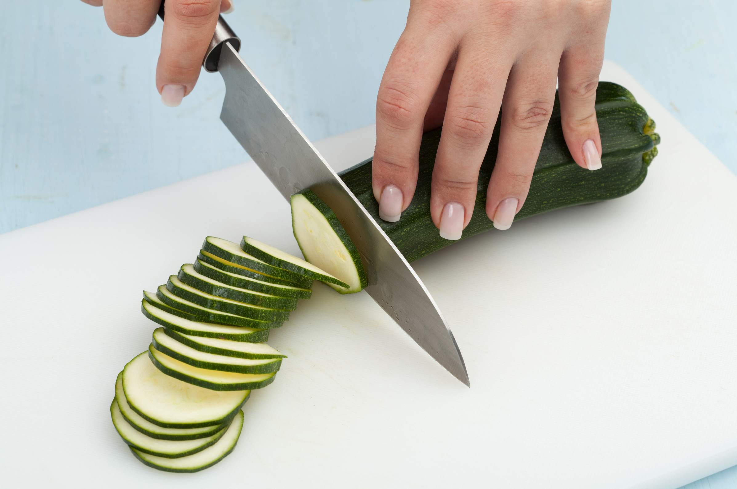 Image of Pro Chefly Damascus chef knife slicing zucchini into even rounds on a cutting board with precise hand control.