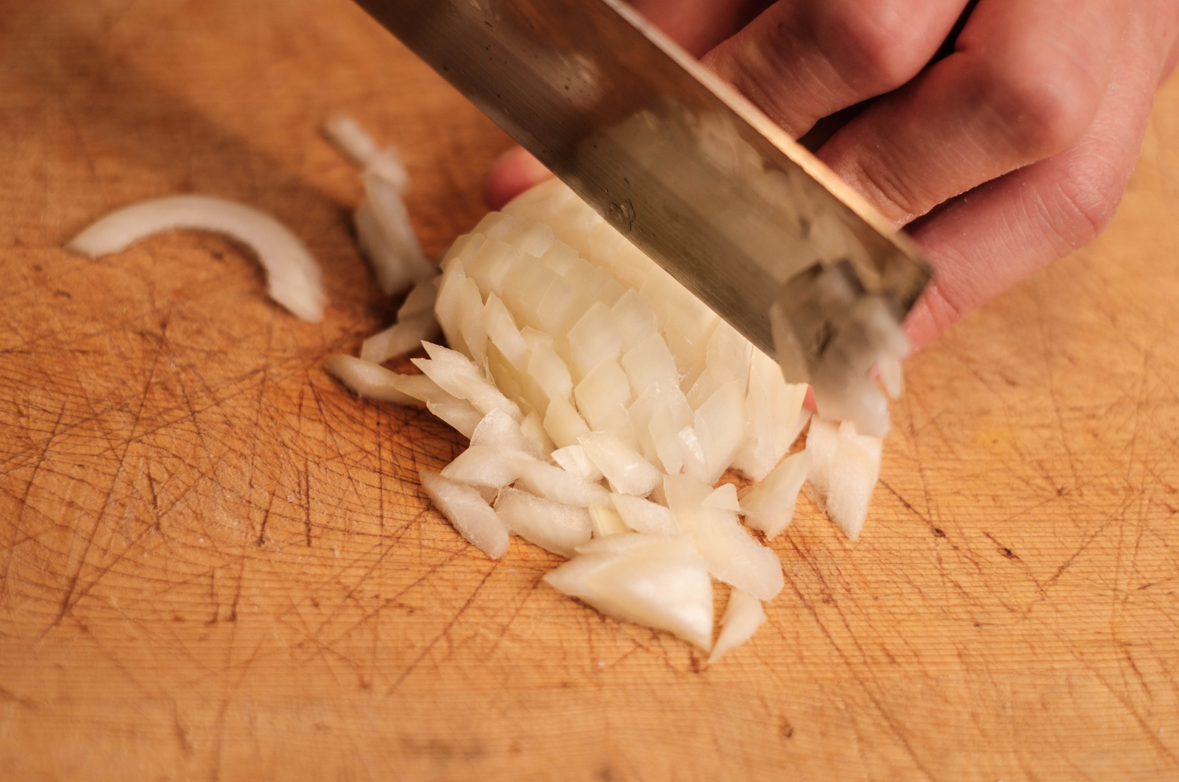 Image of Nakiri knife finely dicing white onion on a wooden cutting board during food prep