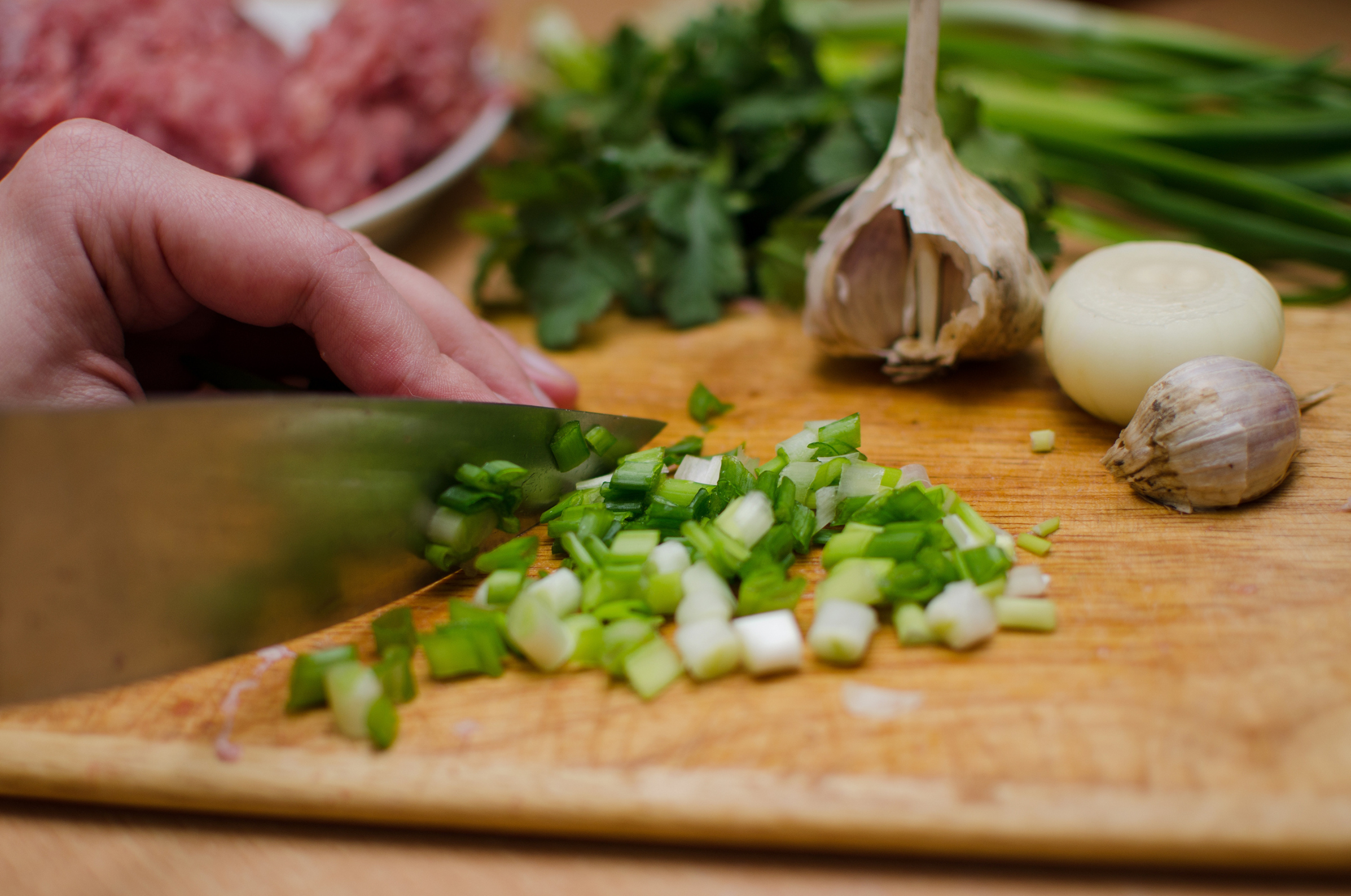 Image of Pro Chefly chef chopping fresh green onions on a wooden cutting board with garlic, onion, and herbs during meal prep