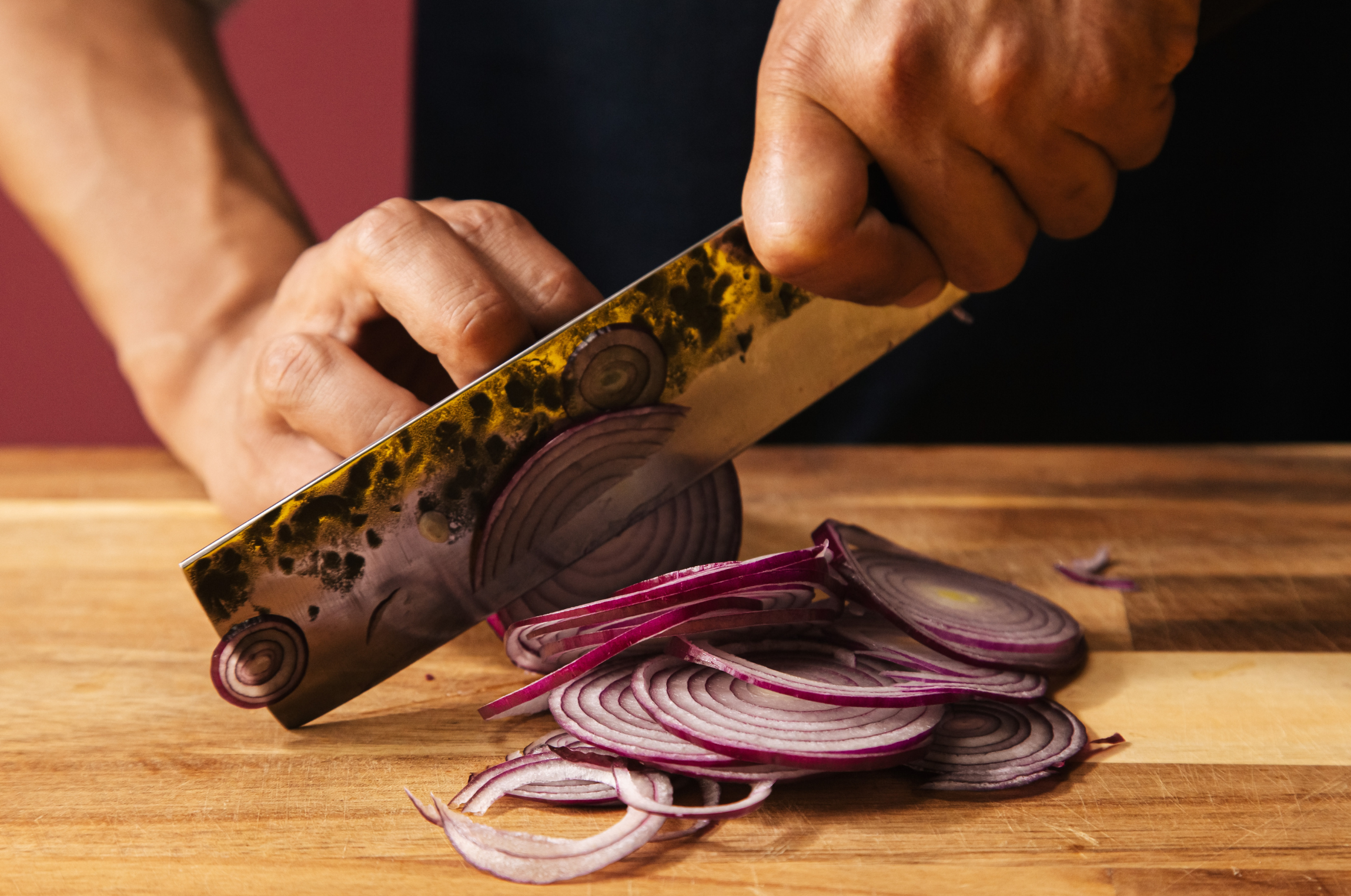 Image of Pro Chefly chef slicing red onion with a Japanese Damascus nakiri knife on a wooden cutting board during food prep