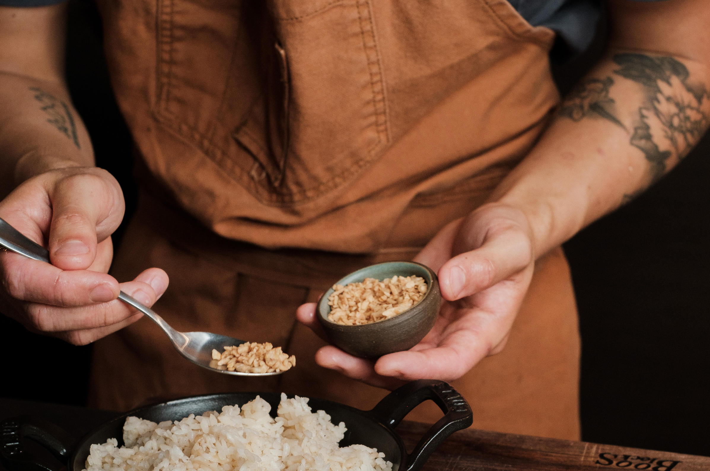 Image of Pro Chefly chef seasoning freshly cooked rice with toasted garlic in a cast iron dish, adding flavor and texture in a warm kitchen setting.