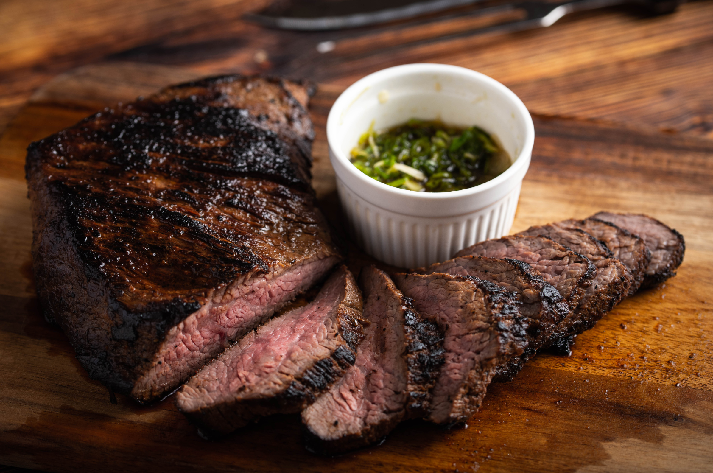 Image of Pro Chefly grilled tri-tip steak sliced medium-rare with a smoky charred crust and fresh herb chimichurri sauce.