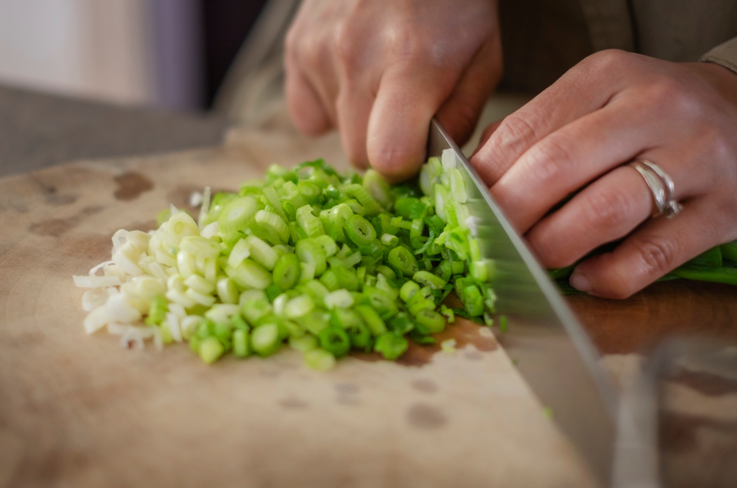 Image of Pro Chefly Japanese chef knife finely slicing fresh green onions on a wooden cutting board with proper pinch grip technique for precision prep.