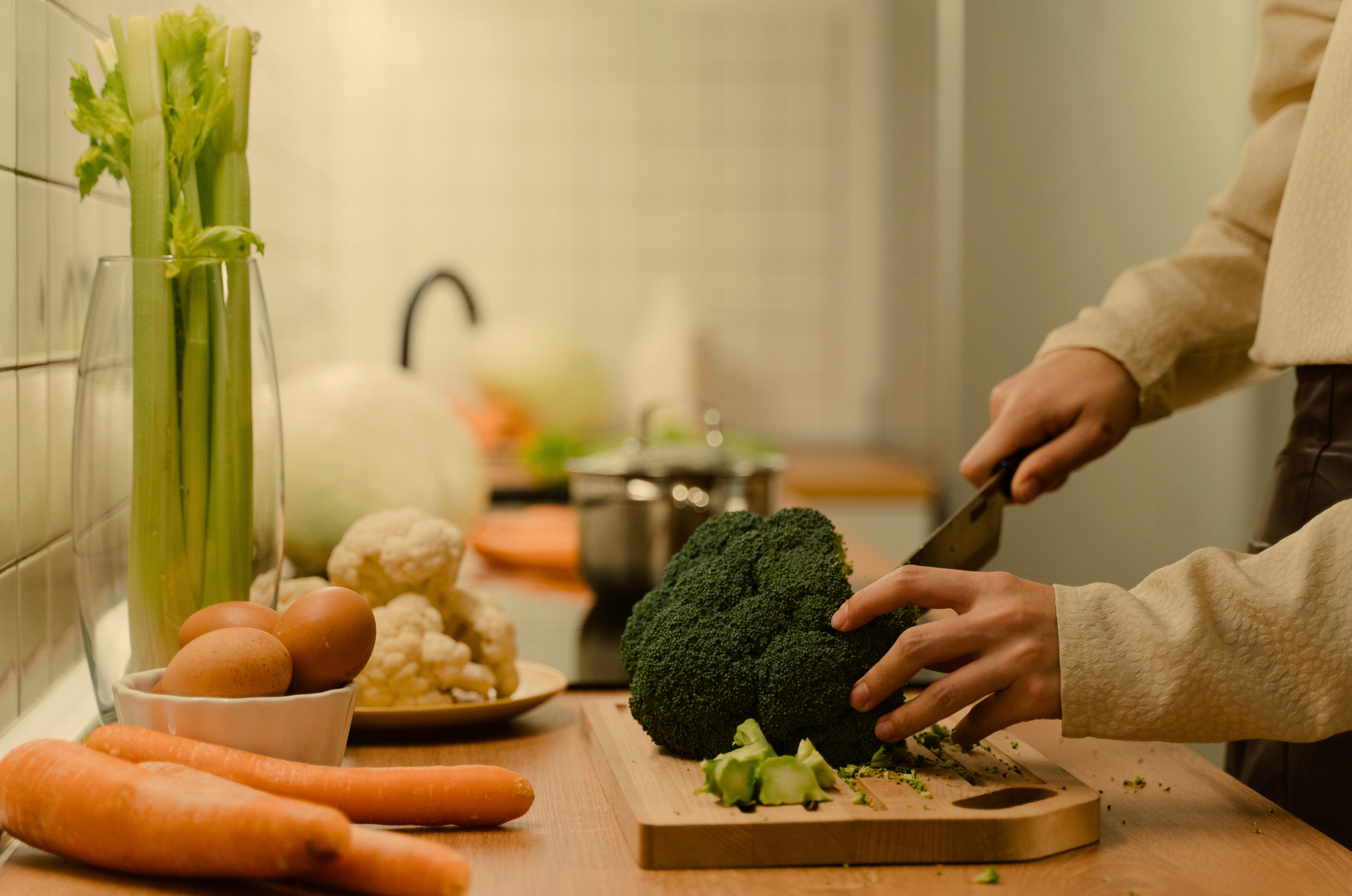 Image of Pro Chefly Japanese knives slicing fresh broccoli on a wooden cutting board in a warm kitchen prep scene.