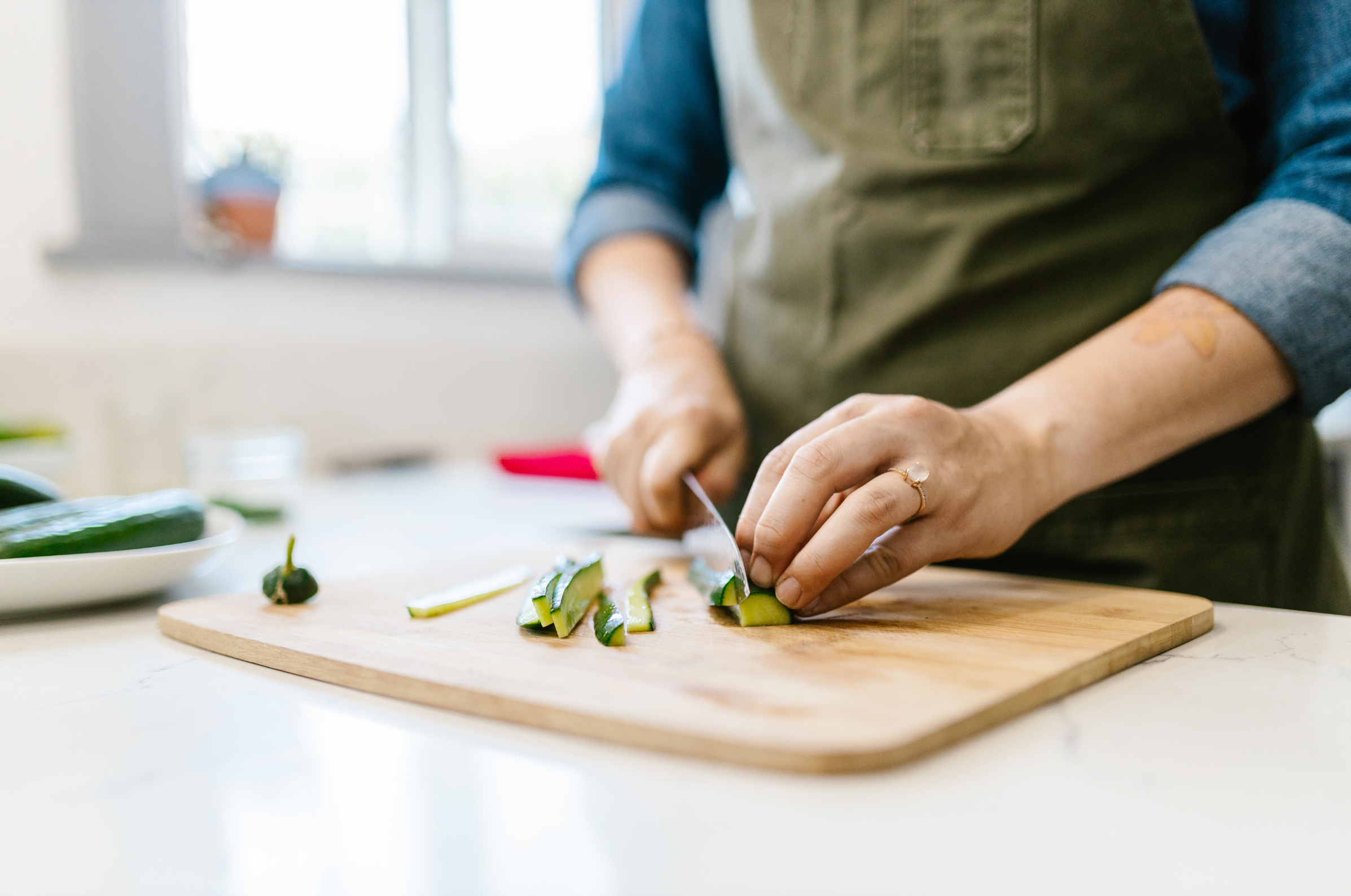 Image of Pro Chefly chef slicing fresh cucumber on a wooden cutting board in a bright home kitchen, food prep photography highlighting knife skills and everyday cooking technique.
