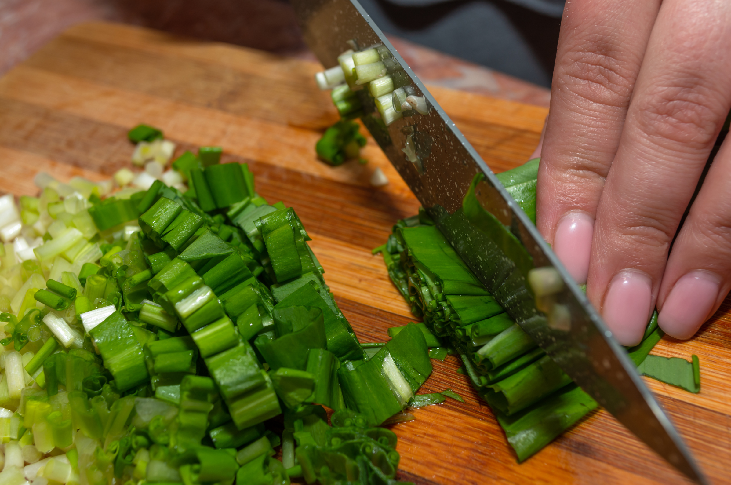 Image of Pro Chefly close-up of fresh green onions being sliced on a wooden cutting board, detailed food prep photography highlighting precision knife skills and ingredient preparation.