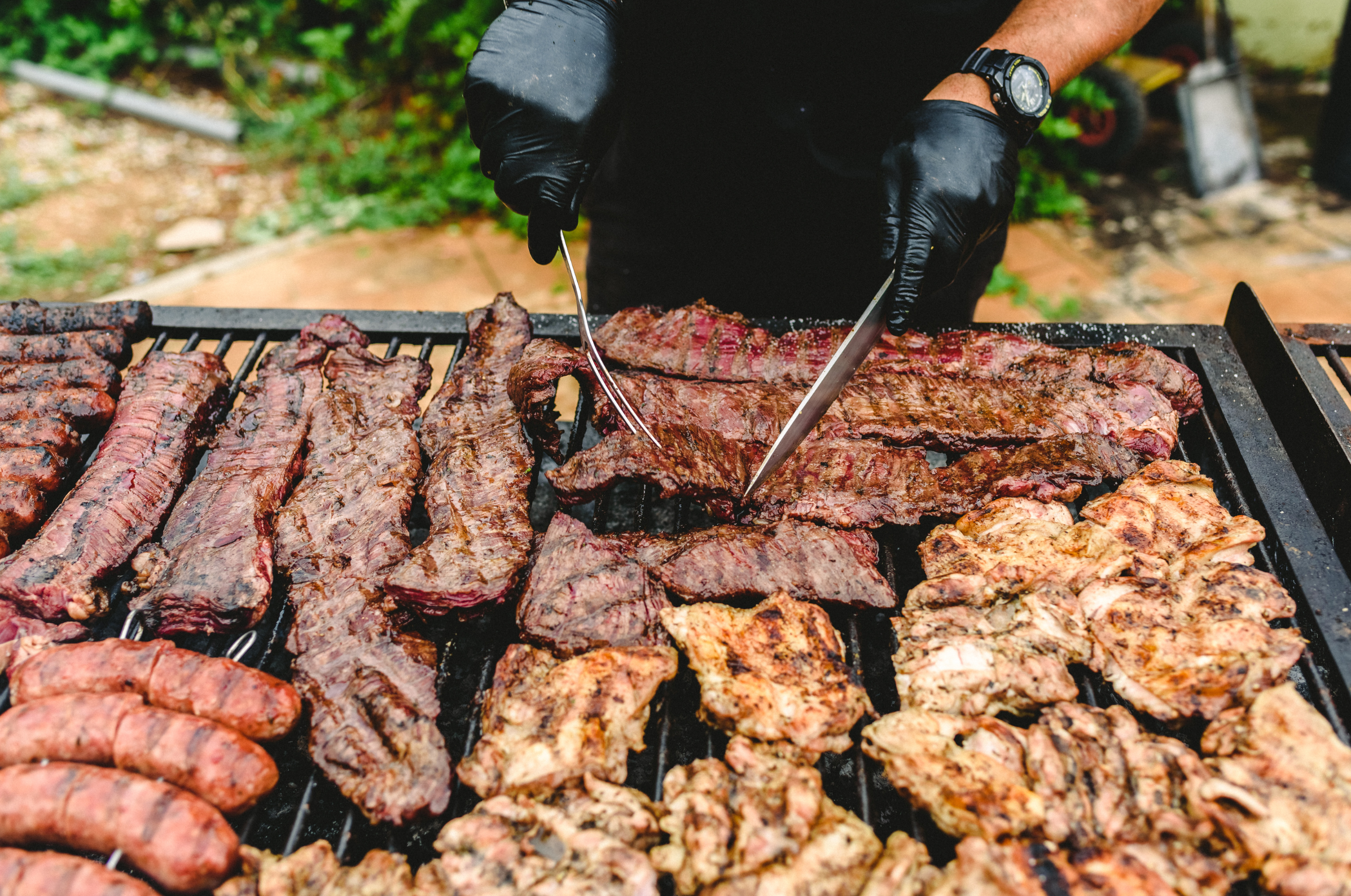 Image of Pro Chefly outdoor grilling spread with sliced steak, grilled chicken, and sausages on the barbecue, live-fire cooking photography highlighting meat preparation and backyard chef craftsmanship.
