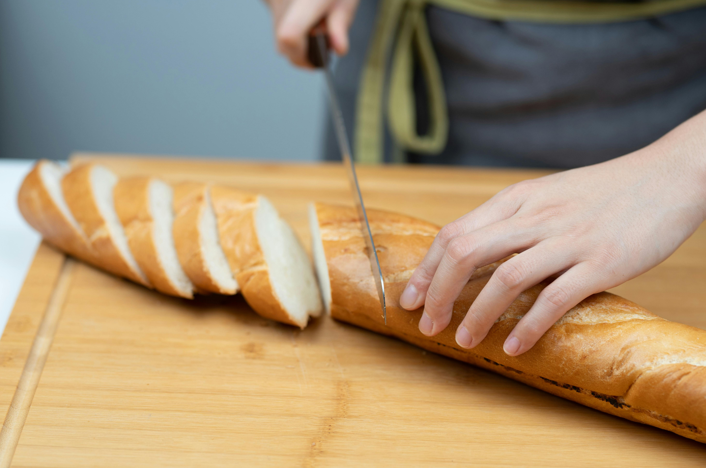 Image of Pro Chefly chef slicing a fresh baguette on a wooden cutting board with a bread knife, creating thick crusty slices for sandwiches, appetizers, or garlic bread.