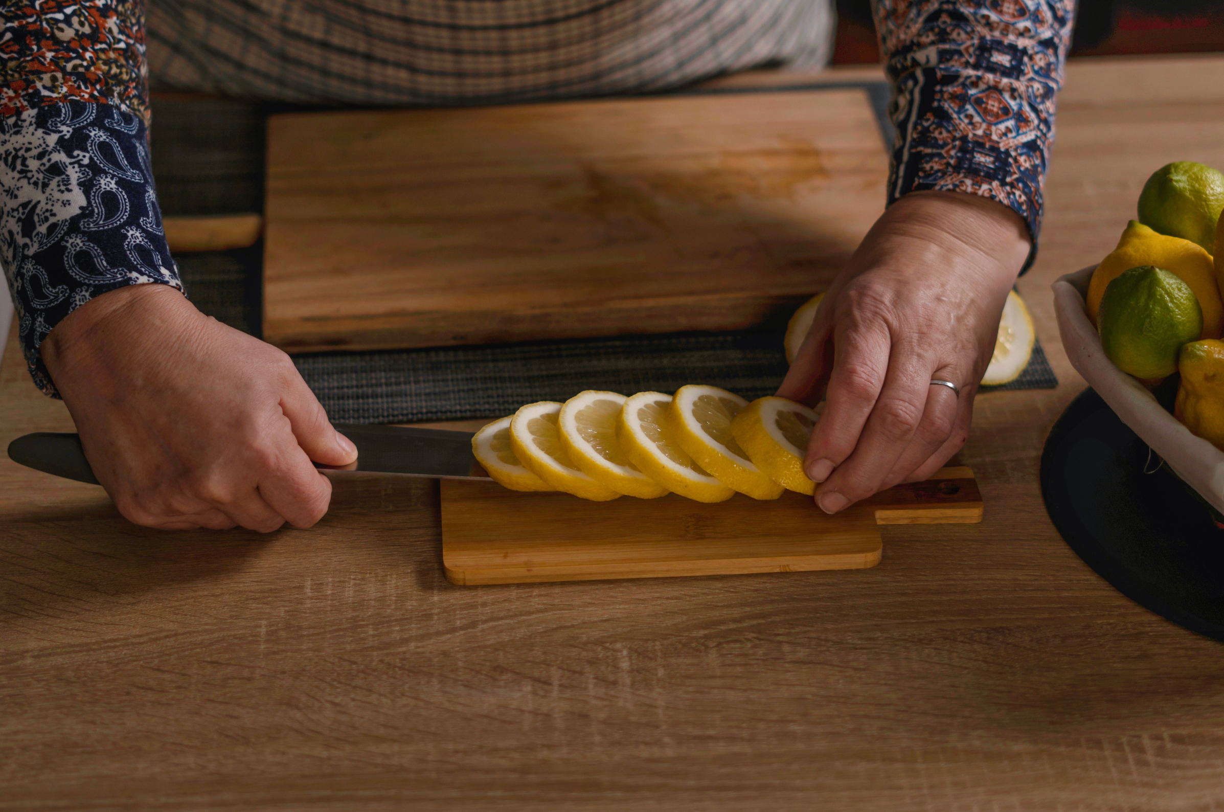 Image of Pro Chefly chef slicing fresh lemon rounds on a wooden cutting board with a chef knife, preparing bright citrus garnish for seafood, grilling, or summer recipes.