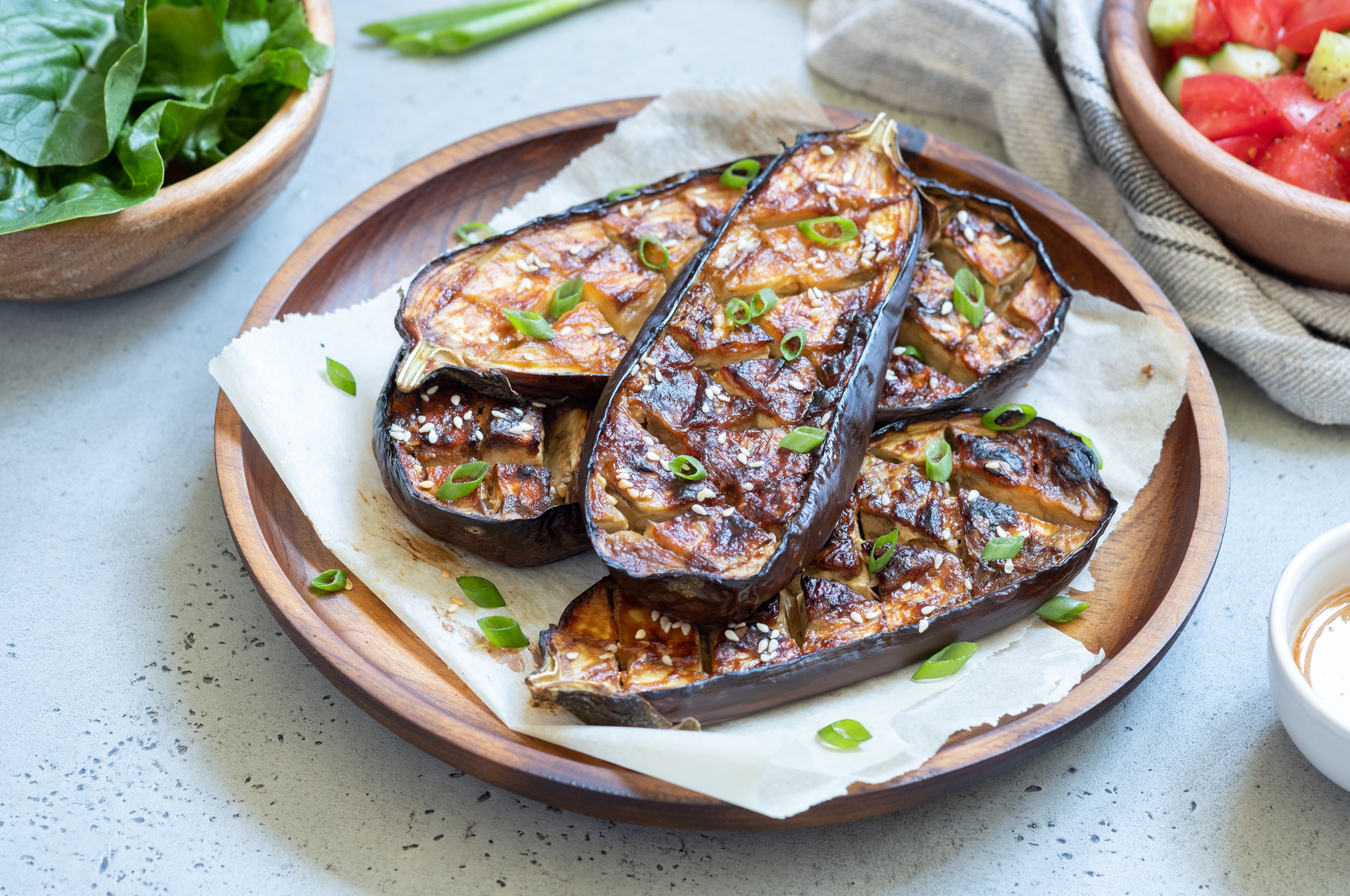 Image of Pro Chefly roasted miso-glazed eggplant halves garnished with sesame seeds and green onions, served on a wooden platter with fresh salad and seasonal vegetables.