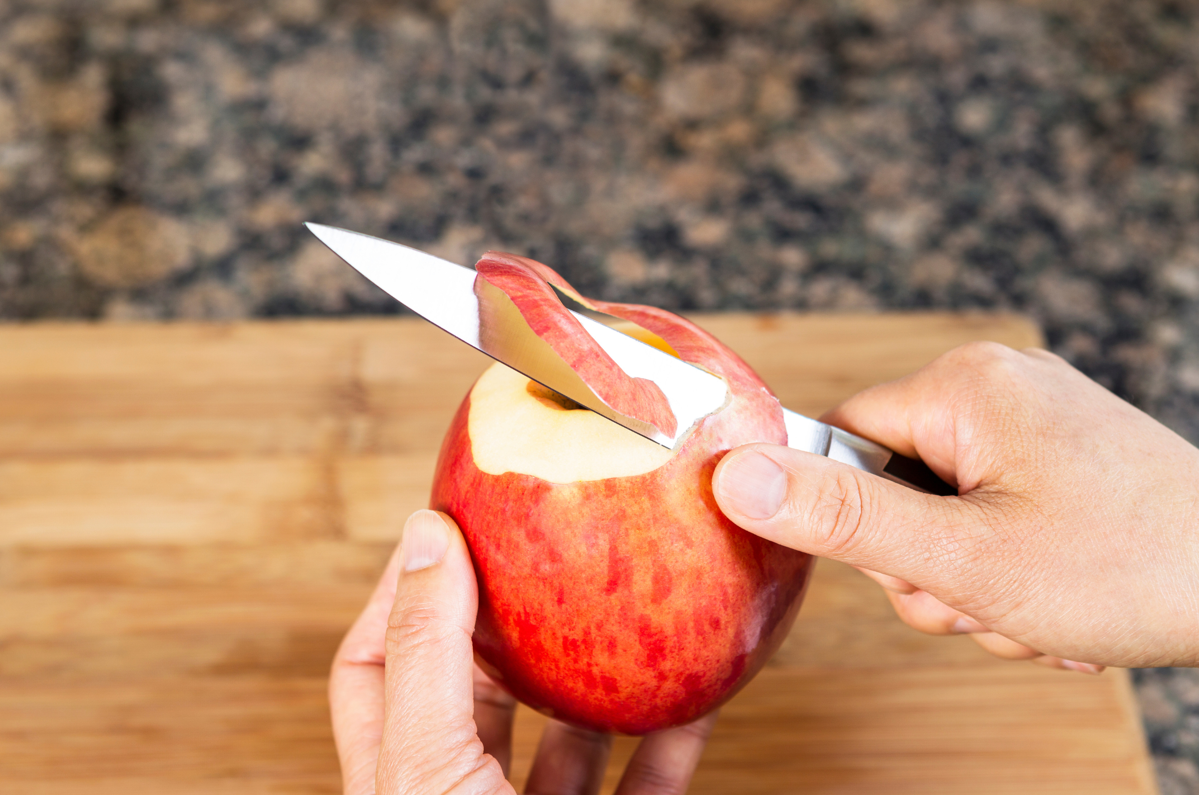 Image of Pro Chefly chef using a paring knife to peel a fresh red apple over a wooden cutting board, demonstrating precise fruit preparation and knife skills.