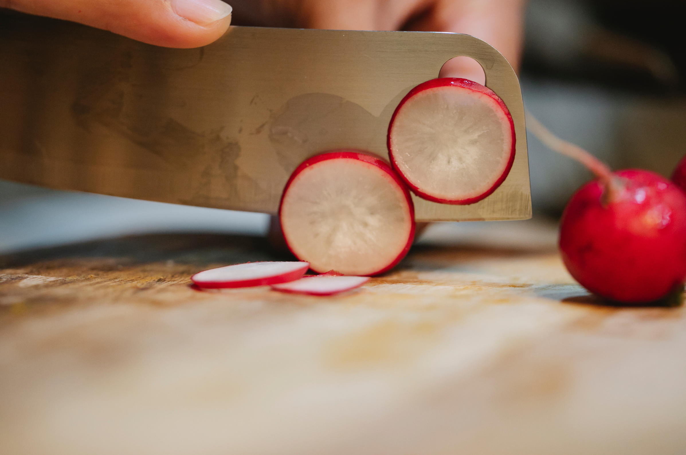 Image of Pro Chefly chef slicing fresh radishes into thin rounds on a wooden cutting board with a precision kitchen knife, highlighting clean cuts and vegetable prep techniques.