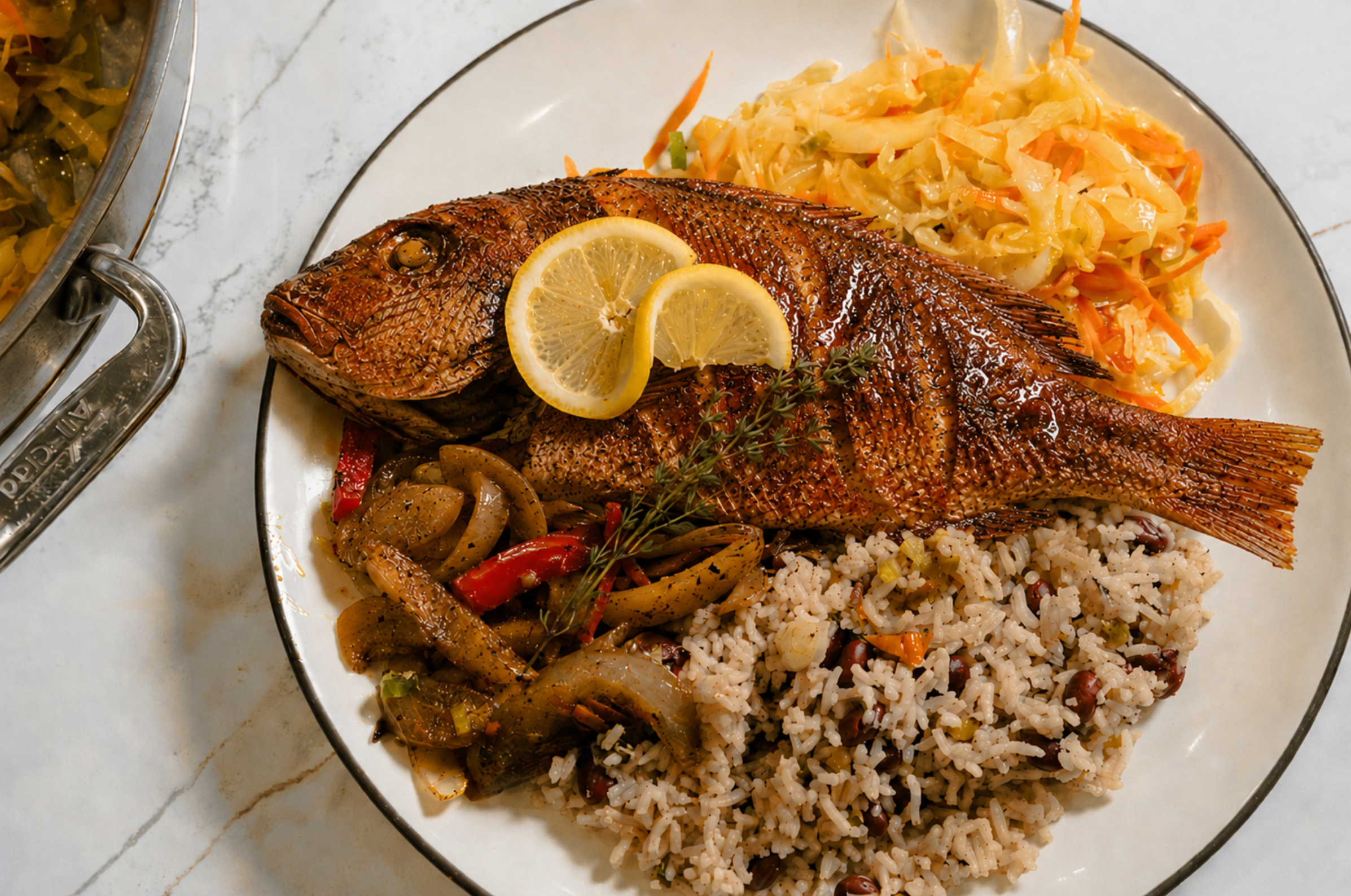 Image of Pro Chefly Jamaican escovitch red snapper served with rice and peas, sautéed vegetables, cabbage slaw, and lemon garnish, authentic Caribbean seafood recipe photography.
