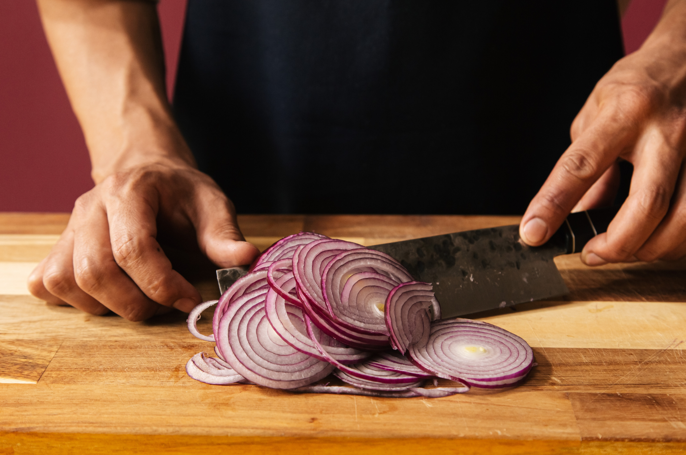 Image of Pro Chefly chef slicing red onion into thin, uniform slices on a wooden cutting board, precision knife skills