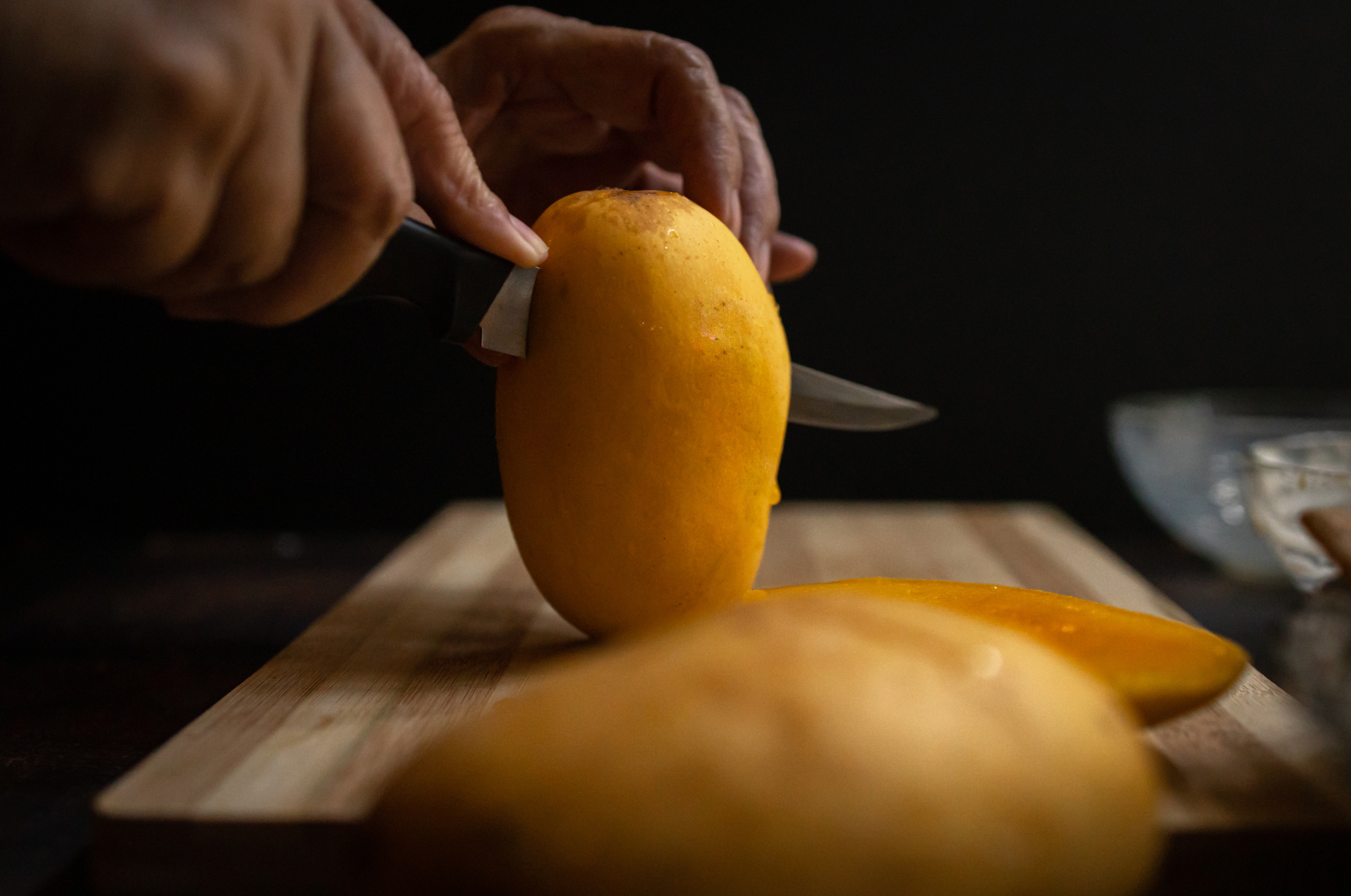 Image of Pro Chefly chef slicing a fresh mango on a wooden cutting board, showcasing precision knife skills and fruit preparation.