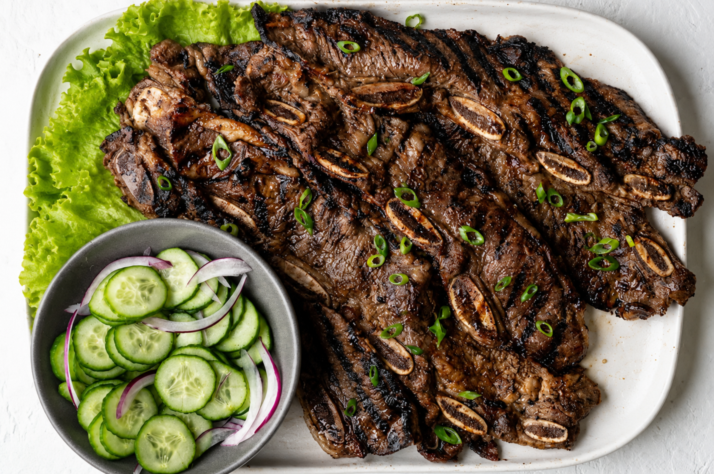 Image of Pro Chefly Korean galbi short ribs grilled over high heat, finished with sliced green onions and served alongside a crisp cucumber salad.