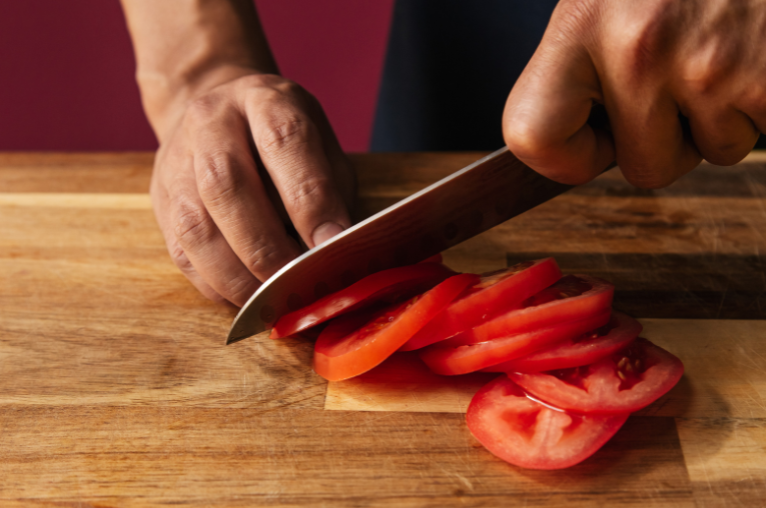 Image of Pro Chefly chef slicing ripe tomatoes on a wooden cutting board, demonstrating precision knife skills and fresh ingredient preparation.