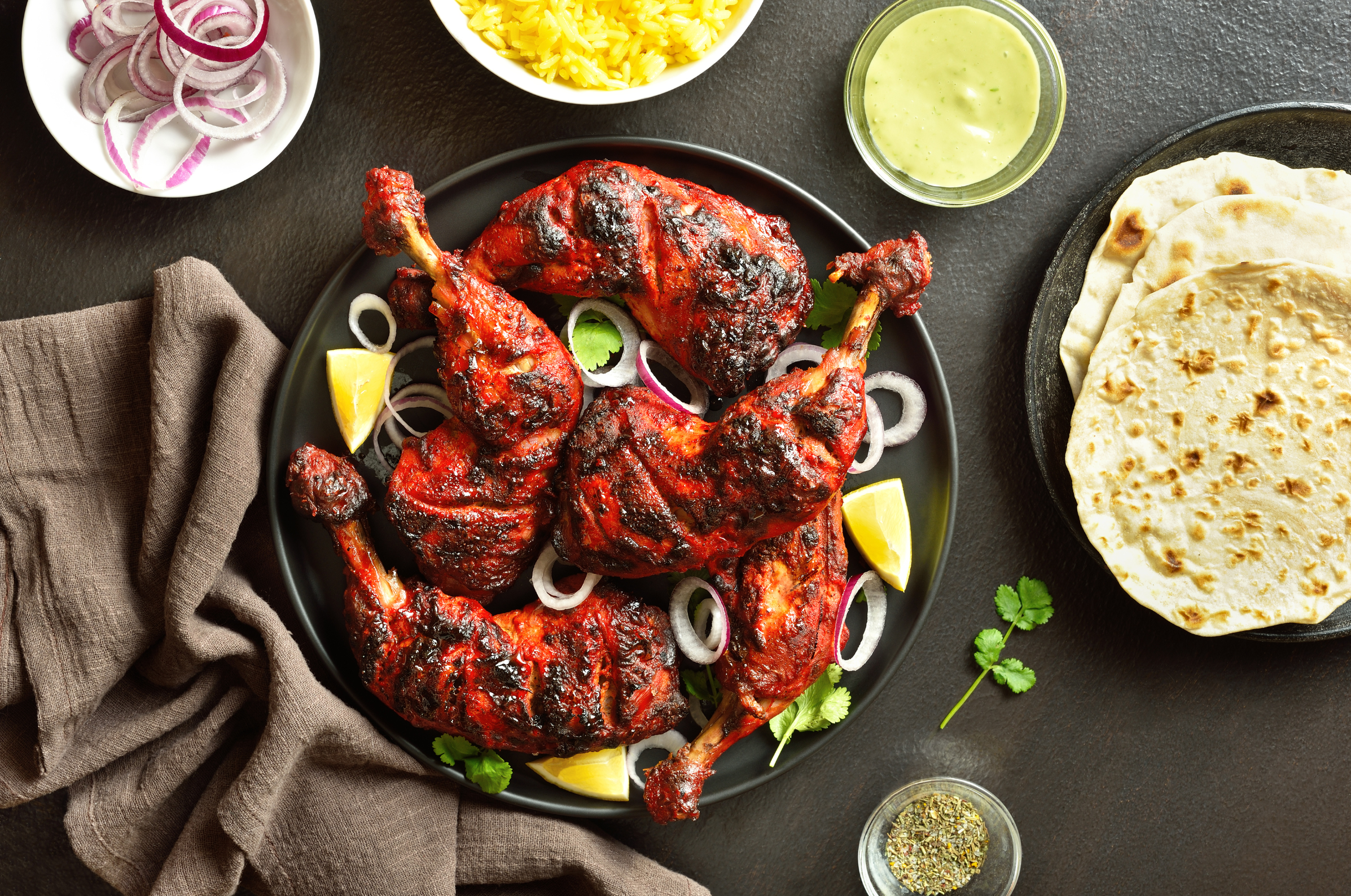 Image of Pro Chefly tandoori grilled chicken with charred yogurt marinade, served with lemon wedges, onions, naan, saffron rice, and creamy cilantro sauce.